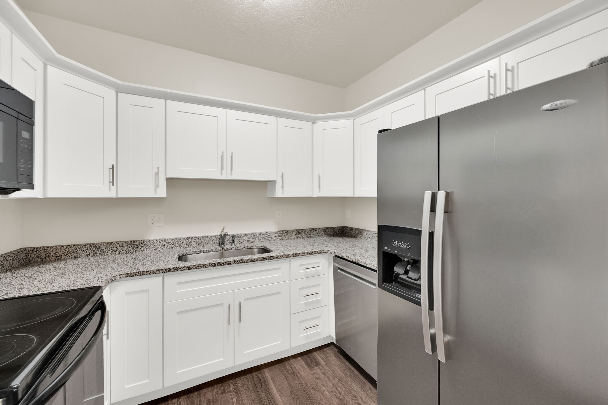 Kitchen featuring white shaker-style cabinetry, granite-finish countertops, stainless steel appliances, and wood-finish flooring