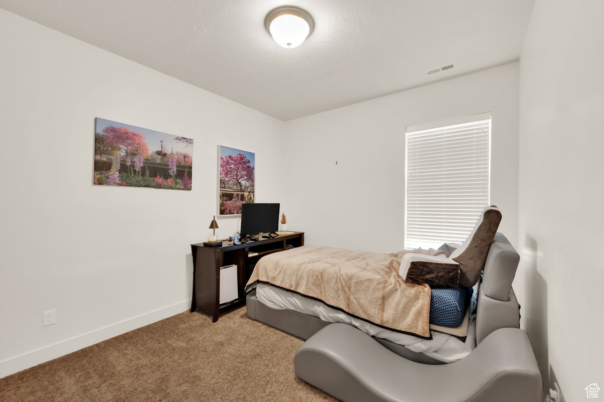 Carpeted room featuring a single window with blinds, white walls, and a ceiling-mounted light fixture