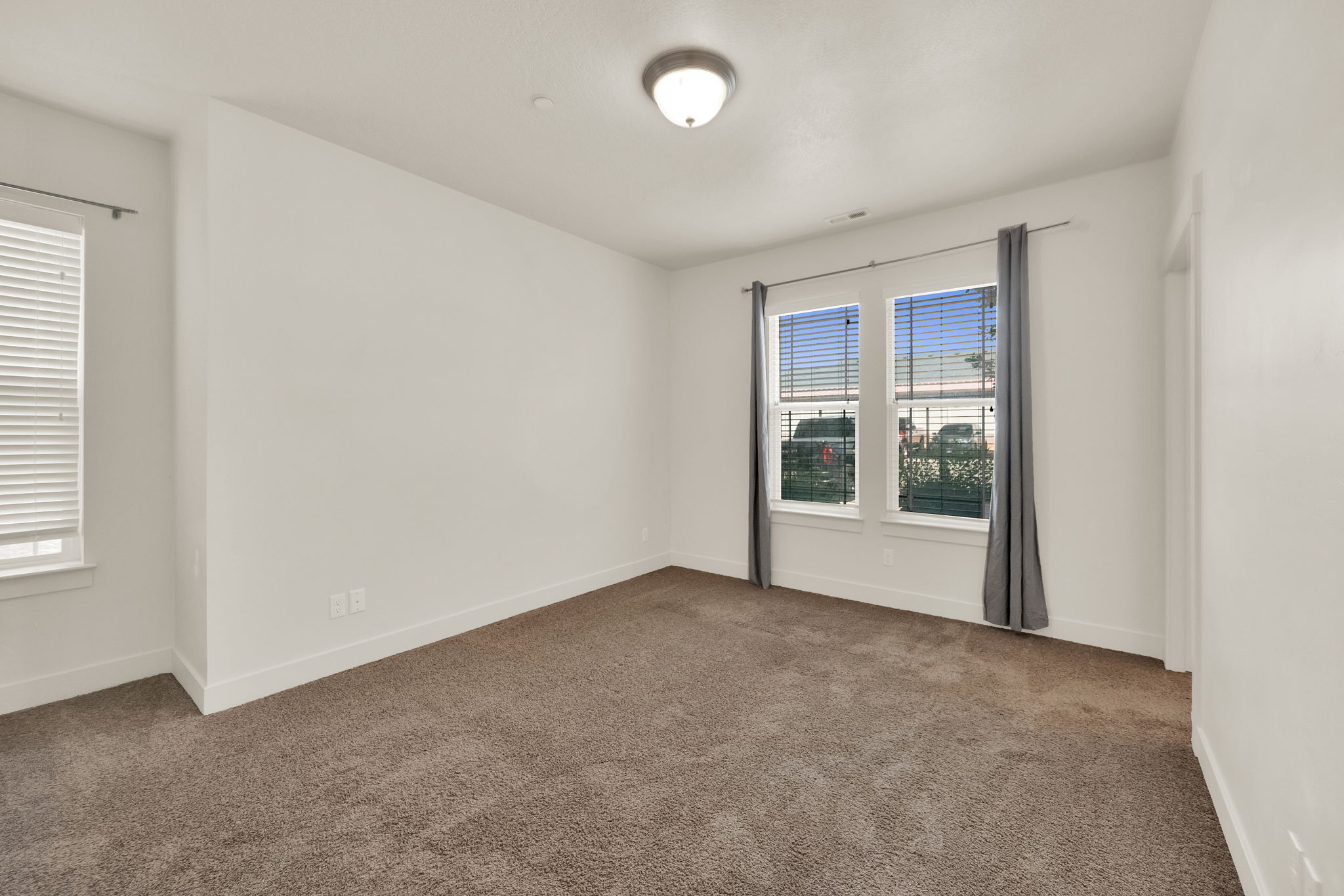Spacious room featuring carpet flooring, crisp white walls, multiple windows with blinds, and an overhead flush mount light fixture