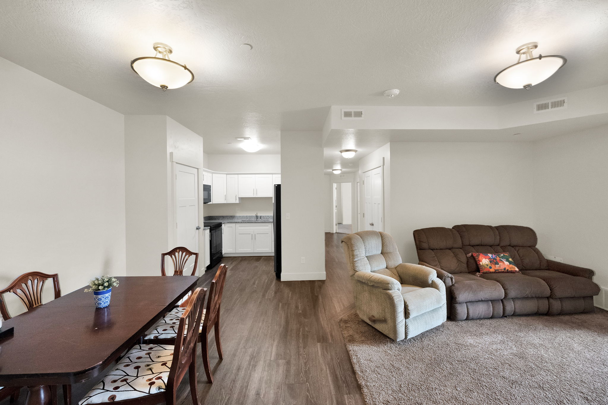 Open-concept interior featuring wood-finish flooring, recessed lighting, and a kitchen with white cabinetry and dark countertops