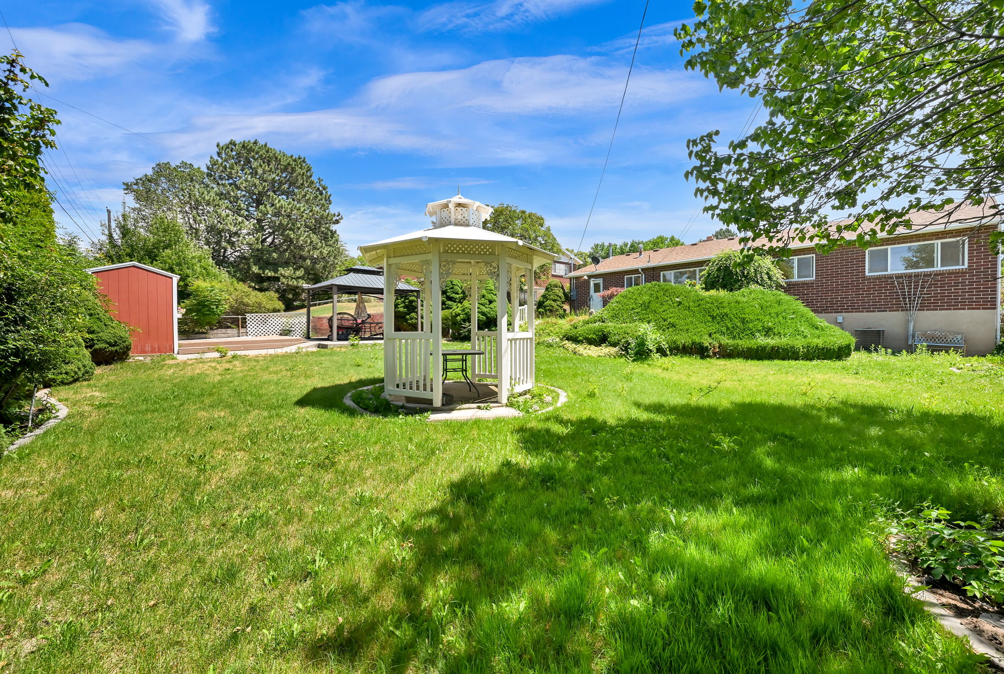 Expansive grassy backyard featuring a white gazebo, a red storage shed, and a wooden deck
