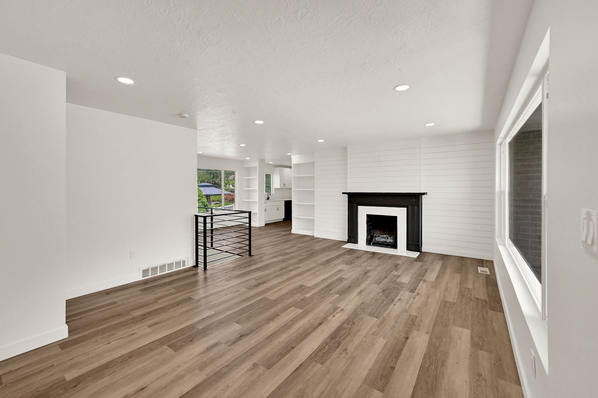 Spacious room featuring wood-finish flooring, recessed lighting, and a black fireplace with a white hearth