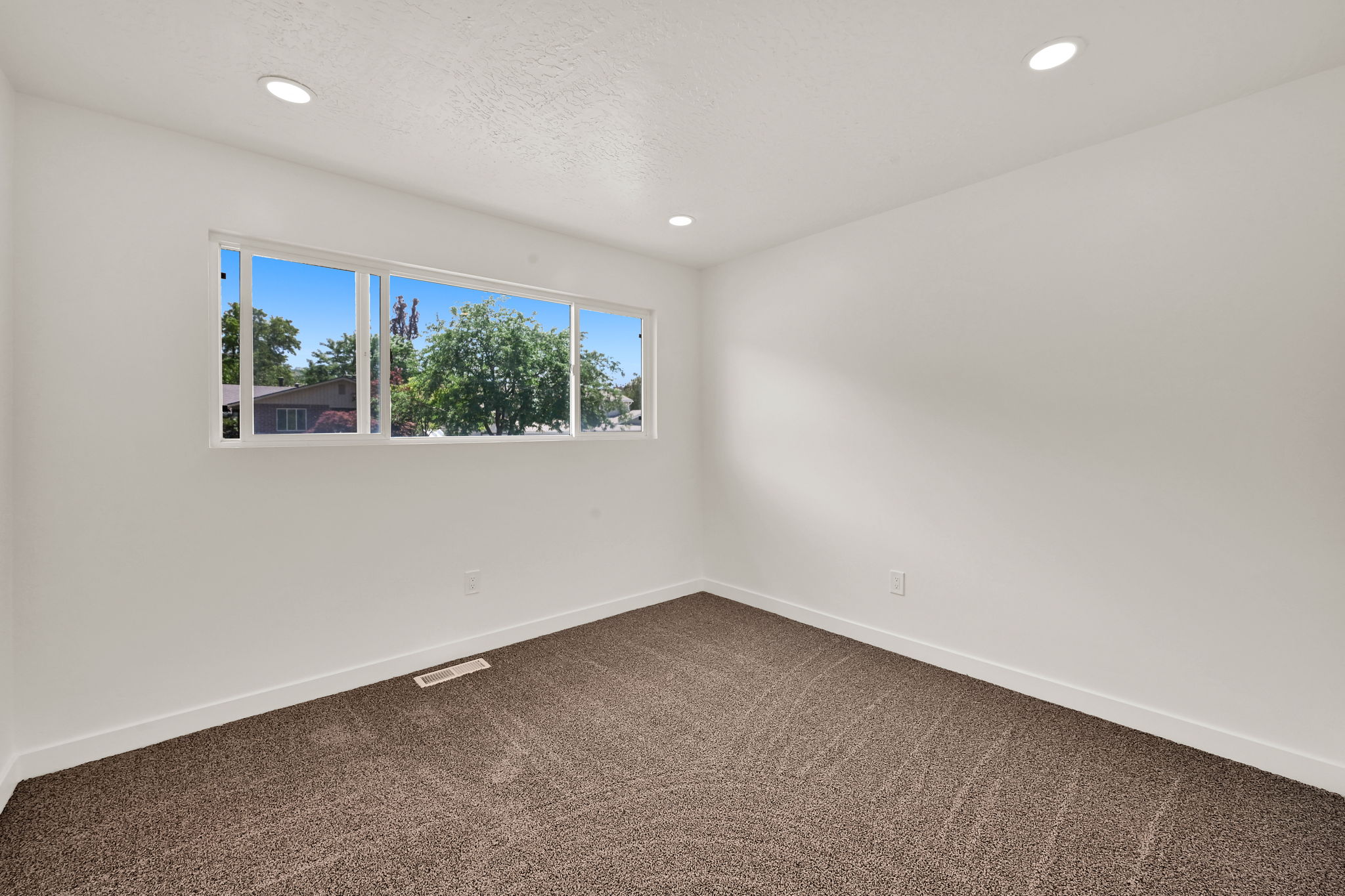 Bright interior space featuring a large horizontal window, recessed ceiling lighting, textured carpet flooring, and white baseboards