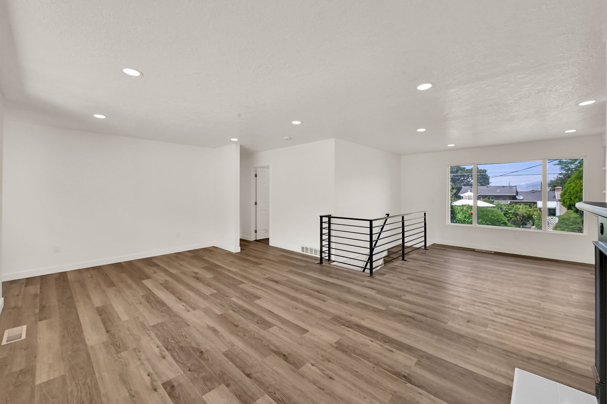 Spacious living area featuring contemporary wood-finish flooring, white walls, and recessed lighting
