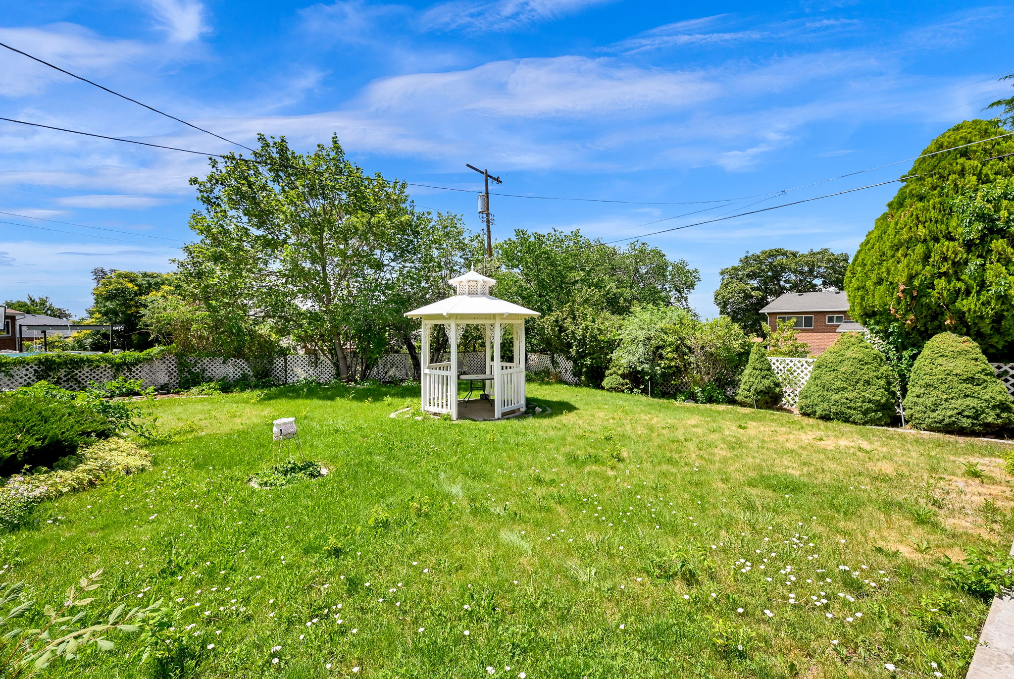 Spacious backyard featuring a white gazebo, mature trees, and a partial lattice fence