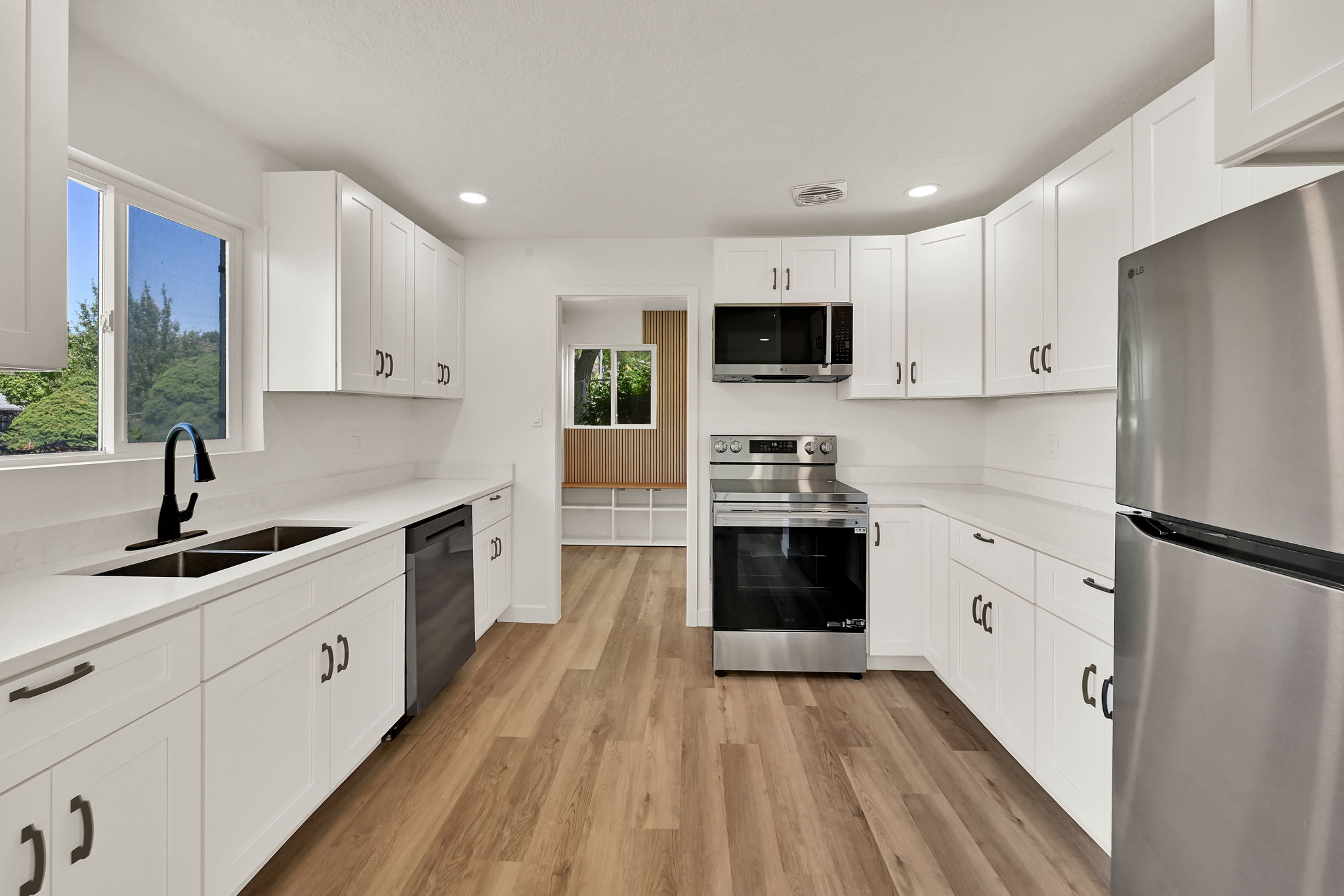 Modern kitchen featuring extensive white cabinetry, light-toned countertops, and wood-finish flooring