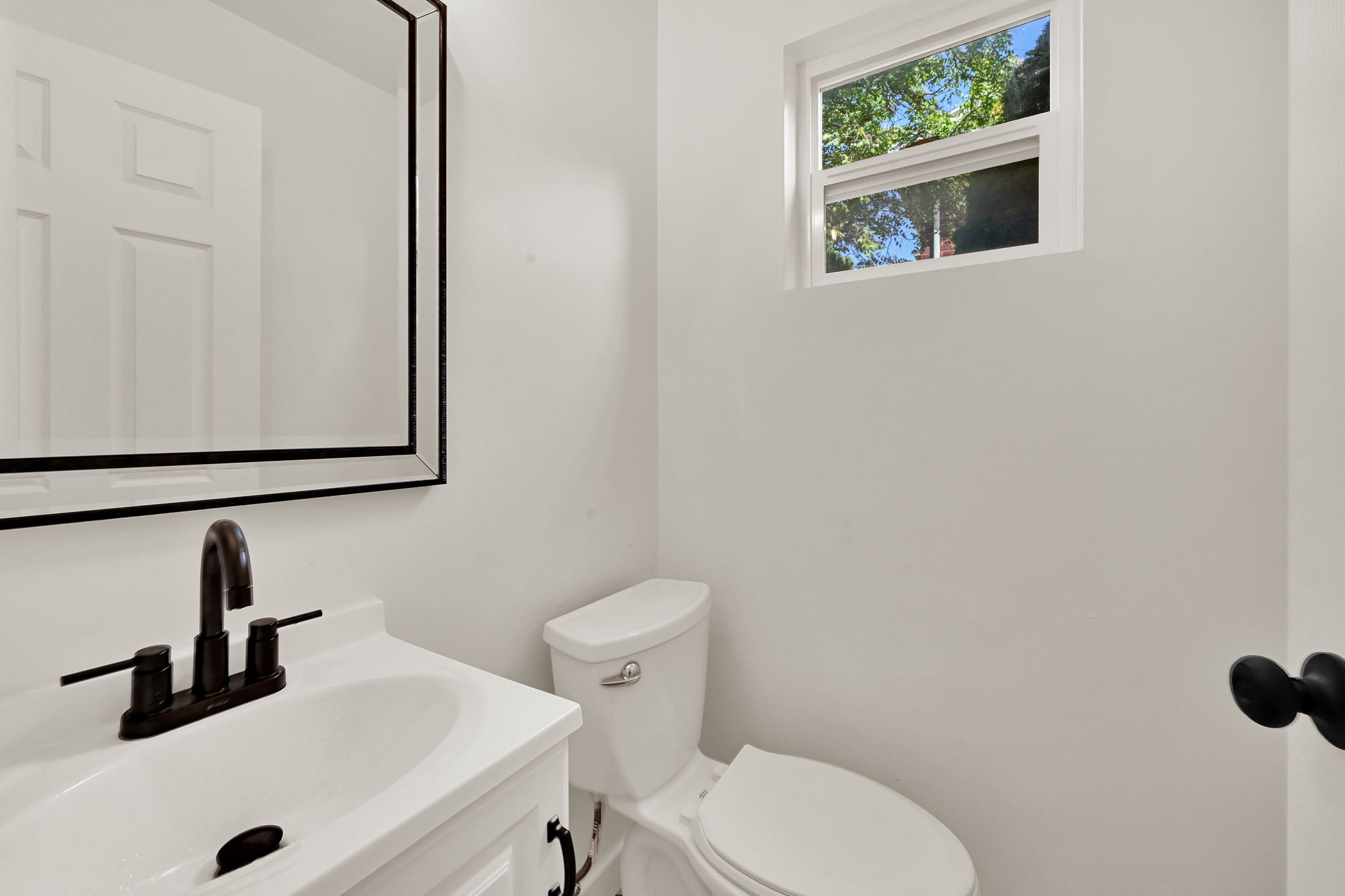 Bathroom featuring a white vanity with an integrated sink, matte black faucet, and a rectangular mirror with a black frame