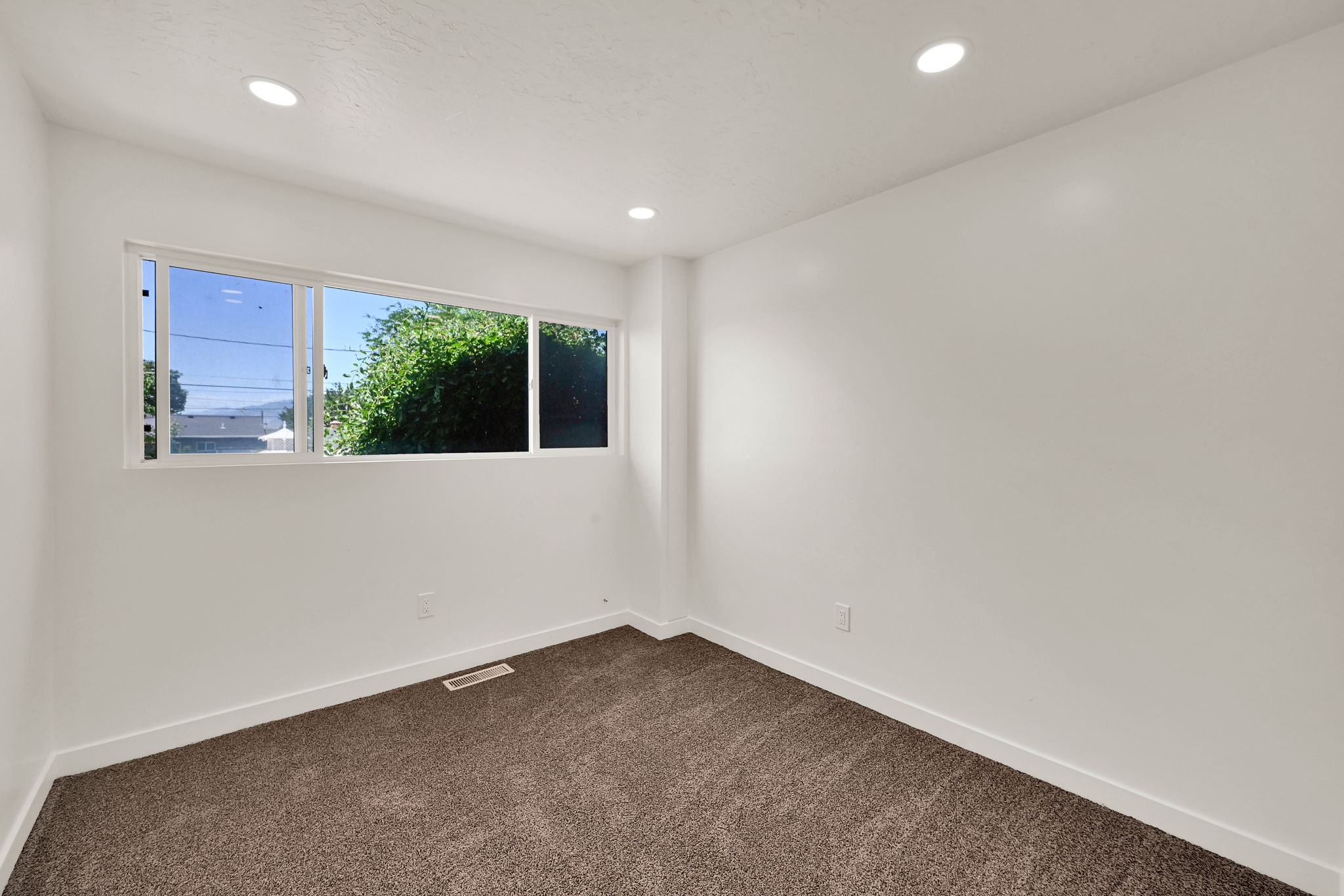 Bright interior space featuring a wide window, recessed ceiling lighting, clean white walls, white baseboards, and brown carpet flooring