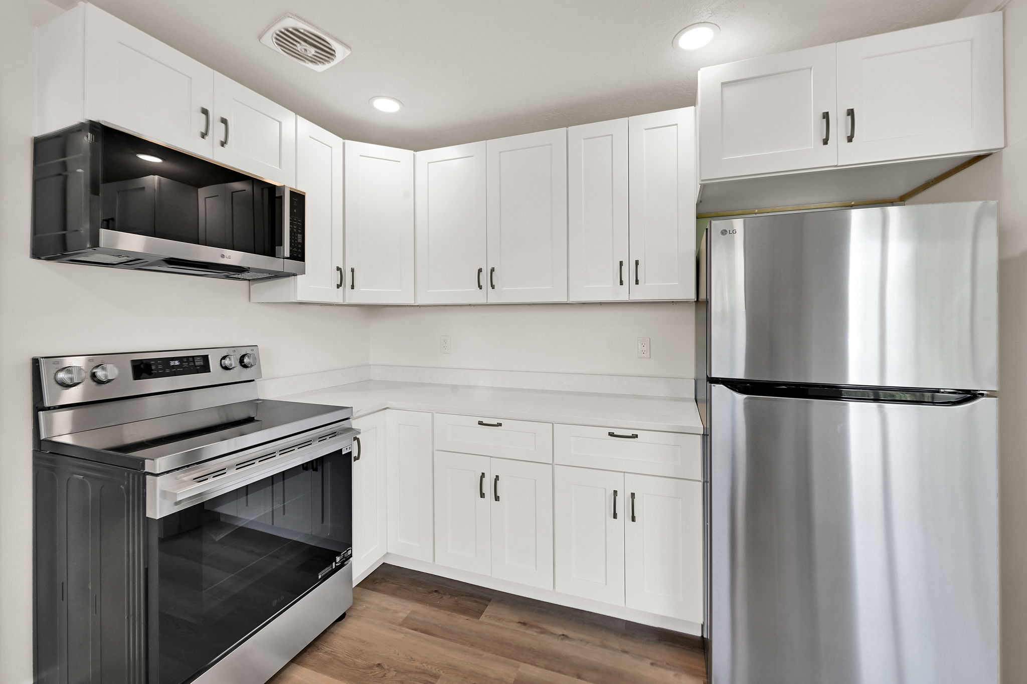Kitchen featuring white shaker cabinetry, stainless steel appliances, light-toned countertops, and wood-finish flooring