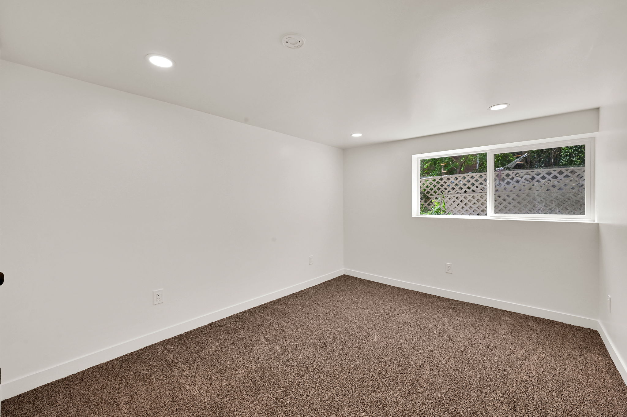 Carpeted room featuring white walls, recessed lighting, and a single window with a lattice-style security grating