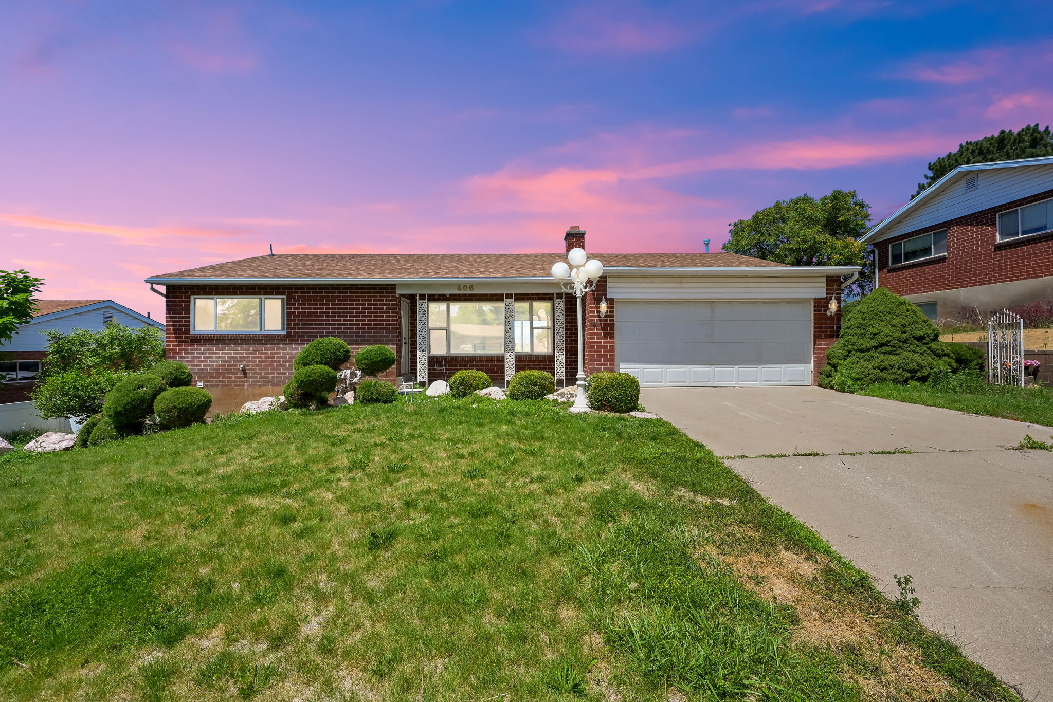 Brick facade residence featuring a front lawn with sculpted shrubbery and a concrete driveway leading to an attached garage