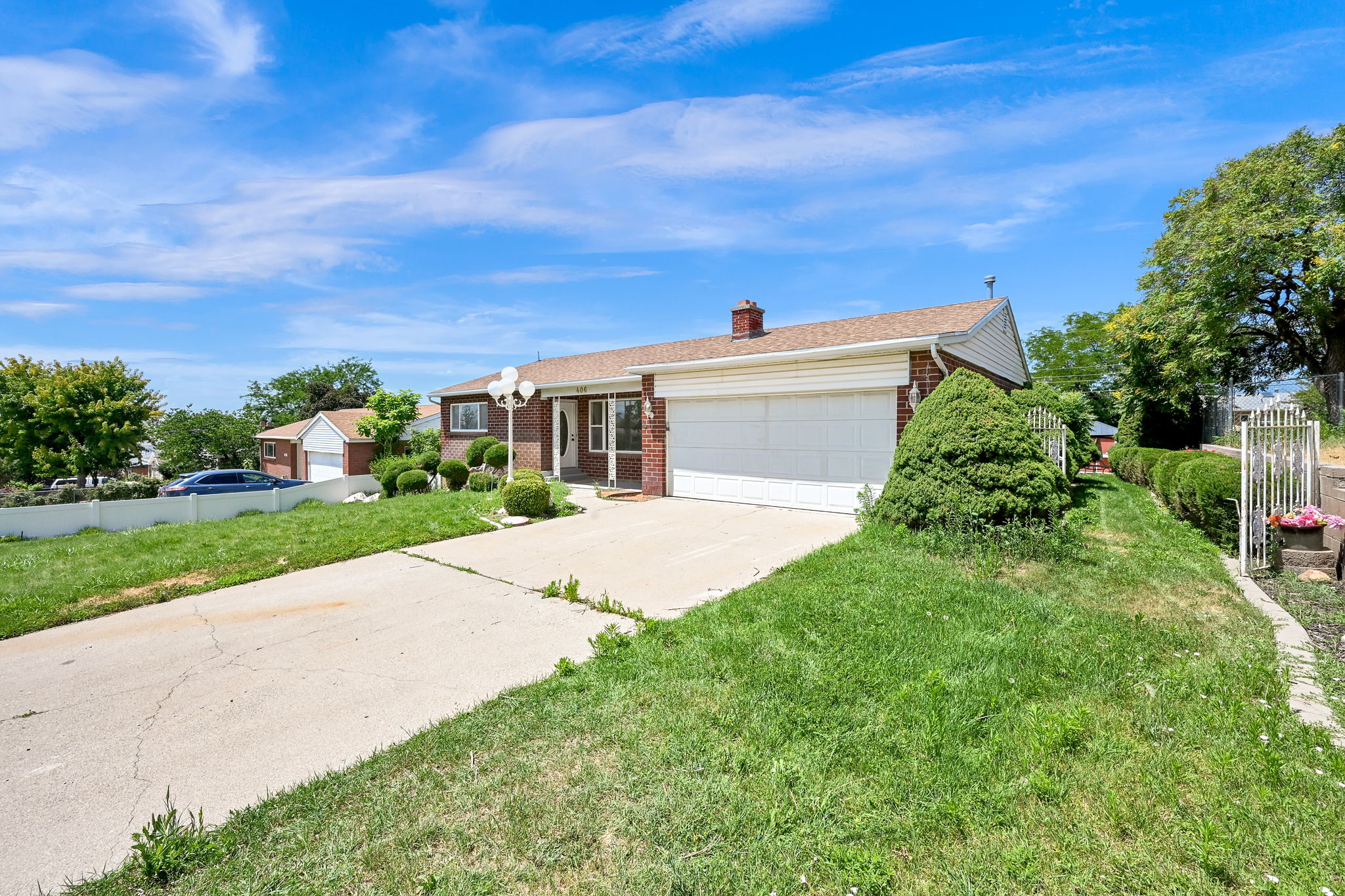 Brick facade residence featuring a two-car garage, concrete driveway, front porch, and mature landscaping