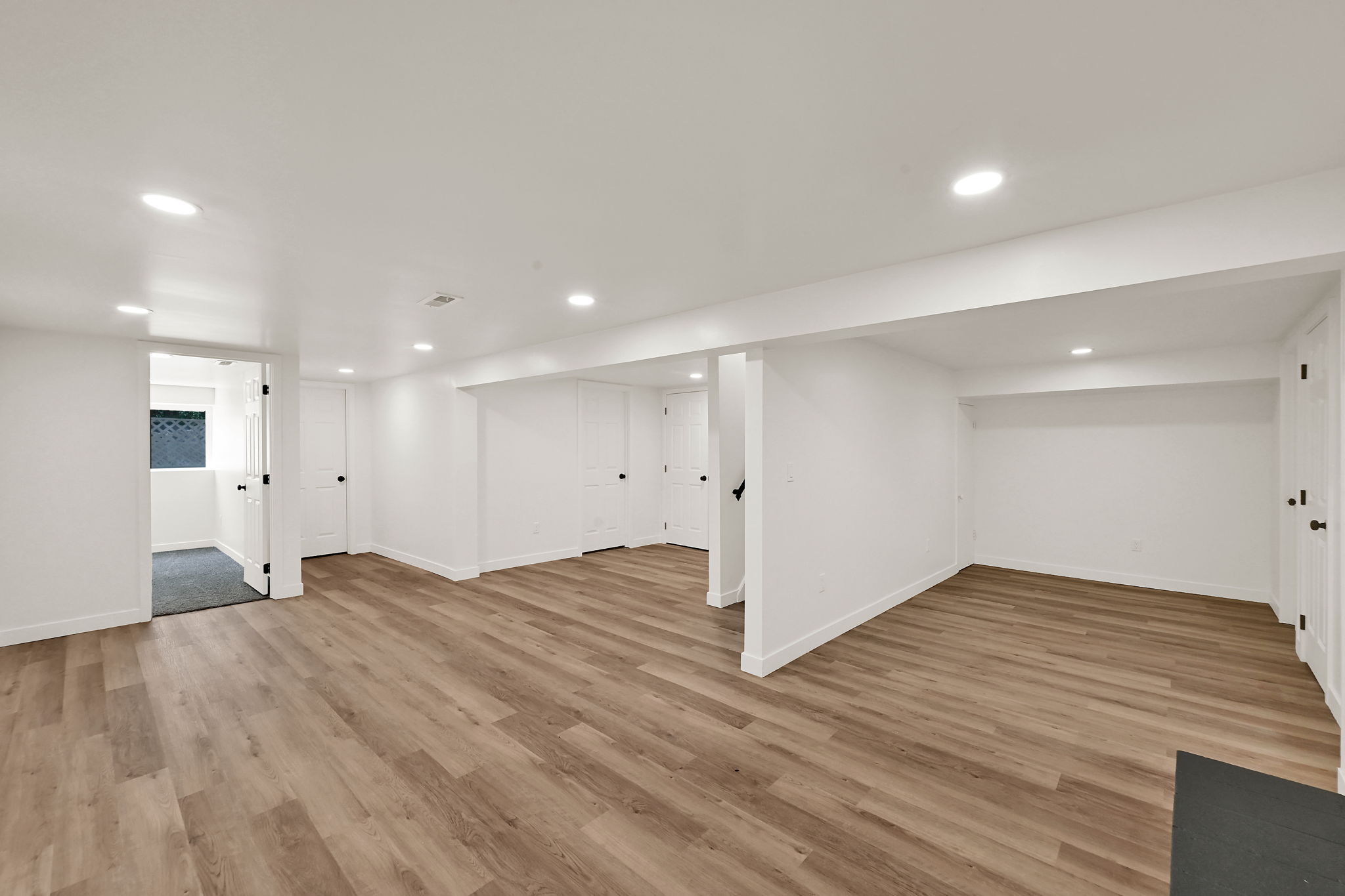 Spacious room featuring wood-finish flooring, recessed lighting, white walls, and multiple white doors with black hardware