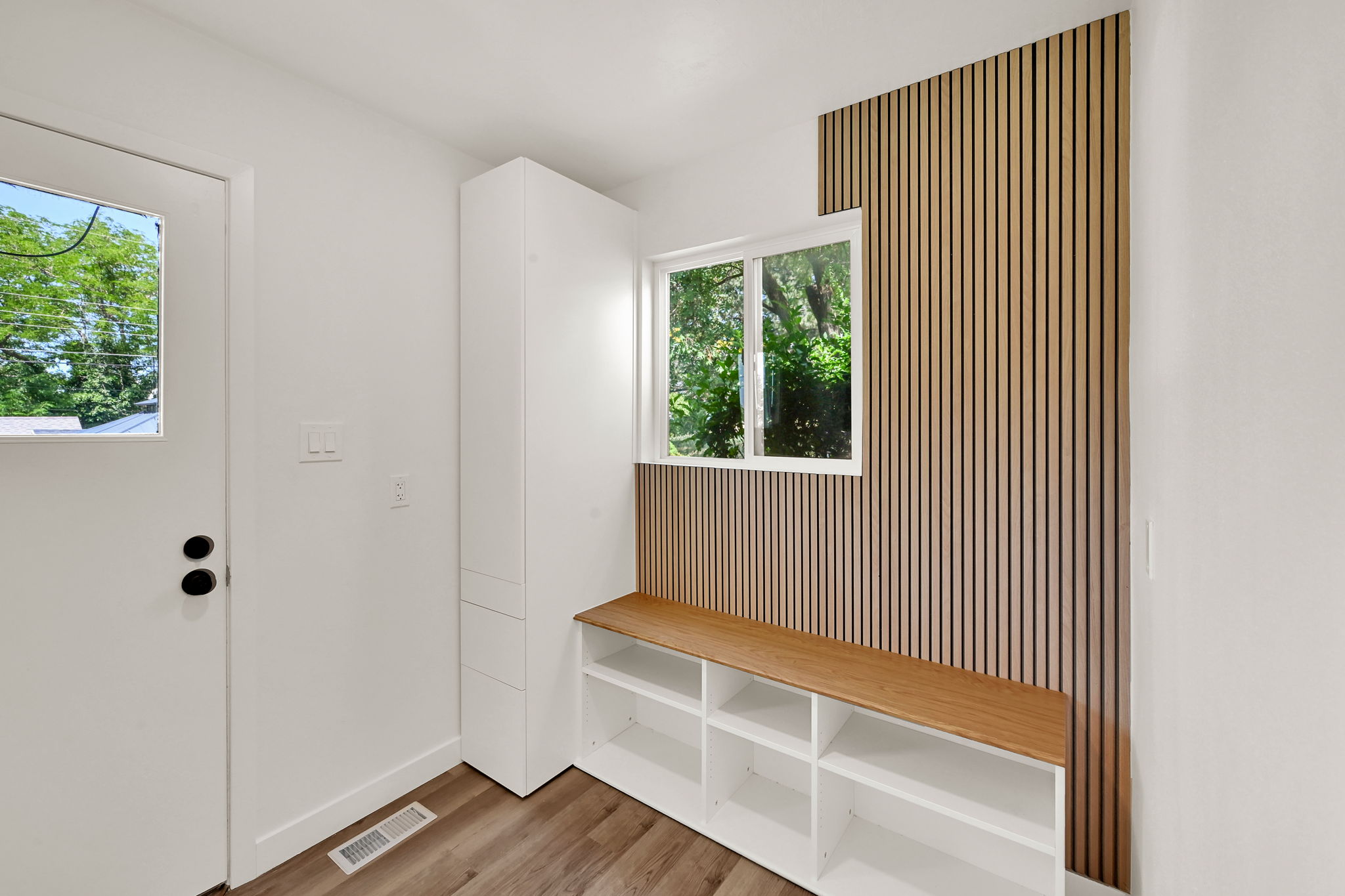 Entryway featuring modern wood slat accent wall, built-in storage bench, and wood-finish flooring