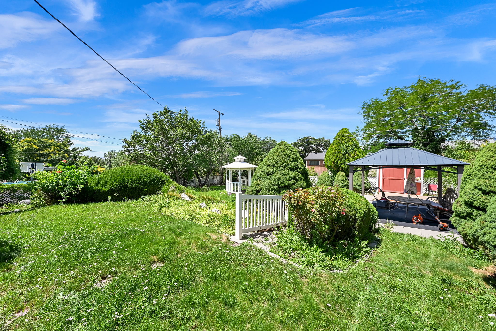 Expansive backyard featuring a gazebo with a gray roof, a white gazebo, a red shed, and mature perimeter trees