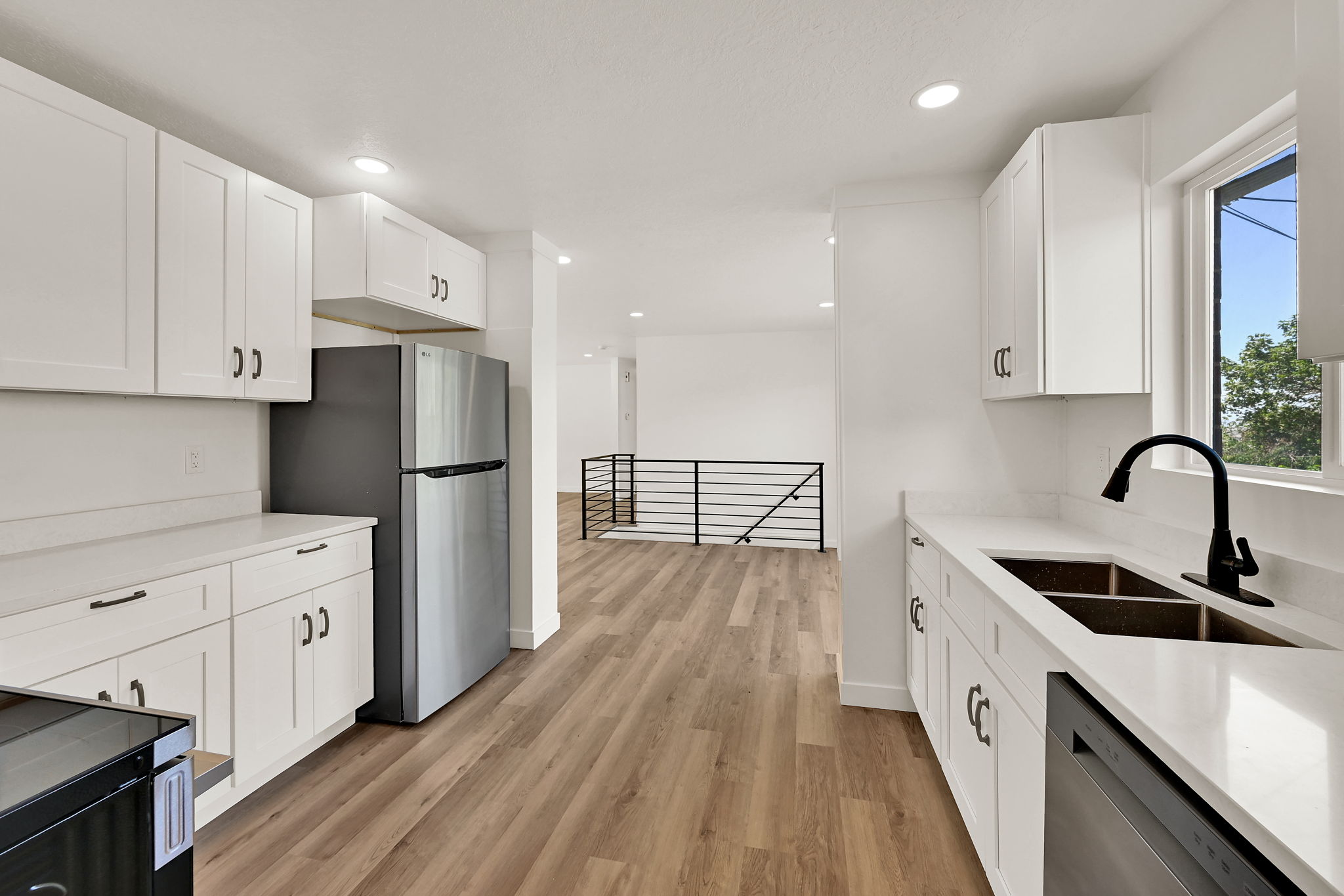 Modern kitchen featuring white cabinetry, light countertops, a stainless steel refrigerator, and wood-finish flooring