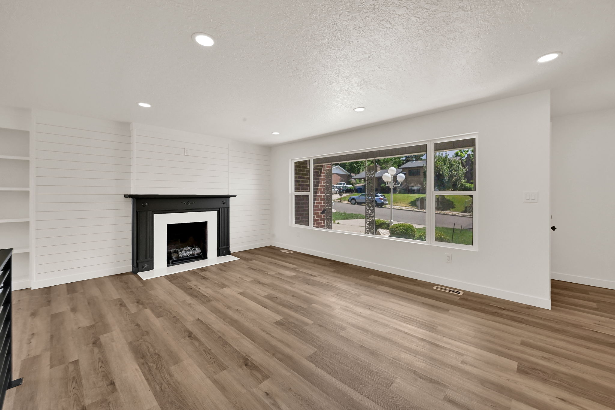 Living area featuring wood-finish flooring, a black mantle fireplace with white surround, recessed lighting, and a prominent shiplap accent wall