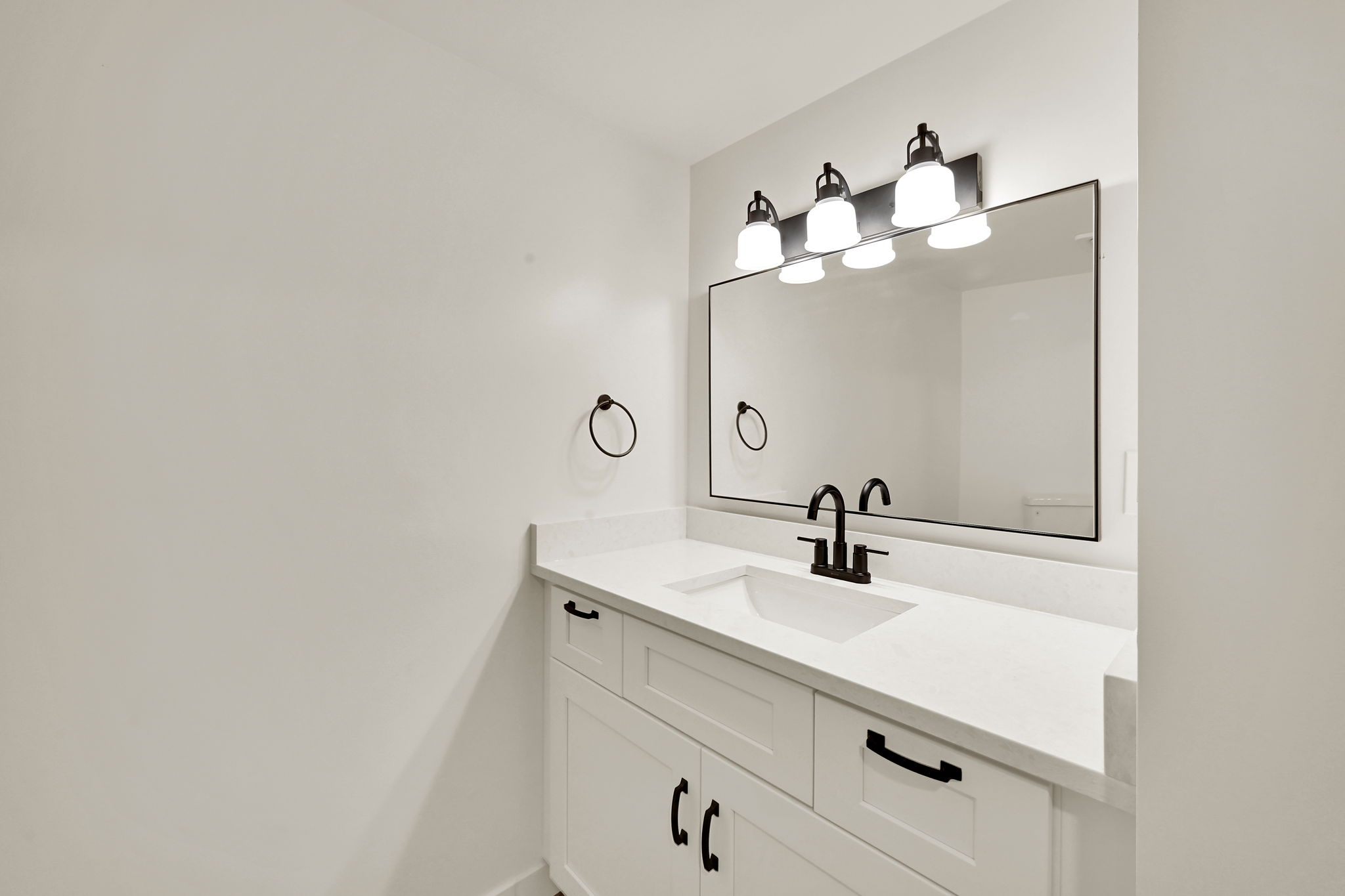 Bright white vanity with a white countertop and integrated sink, featuring a matte black faucet and coordinating mirror