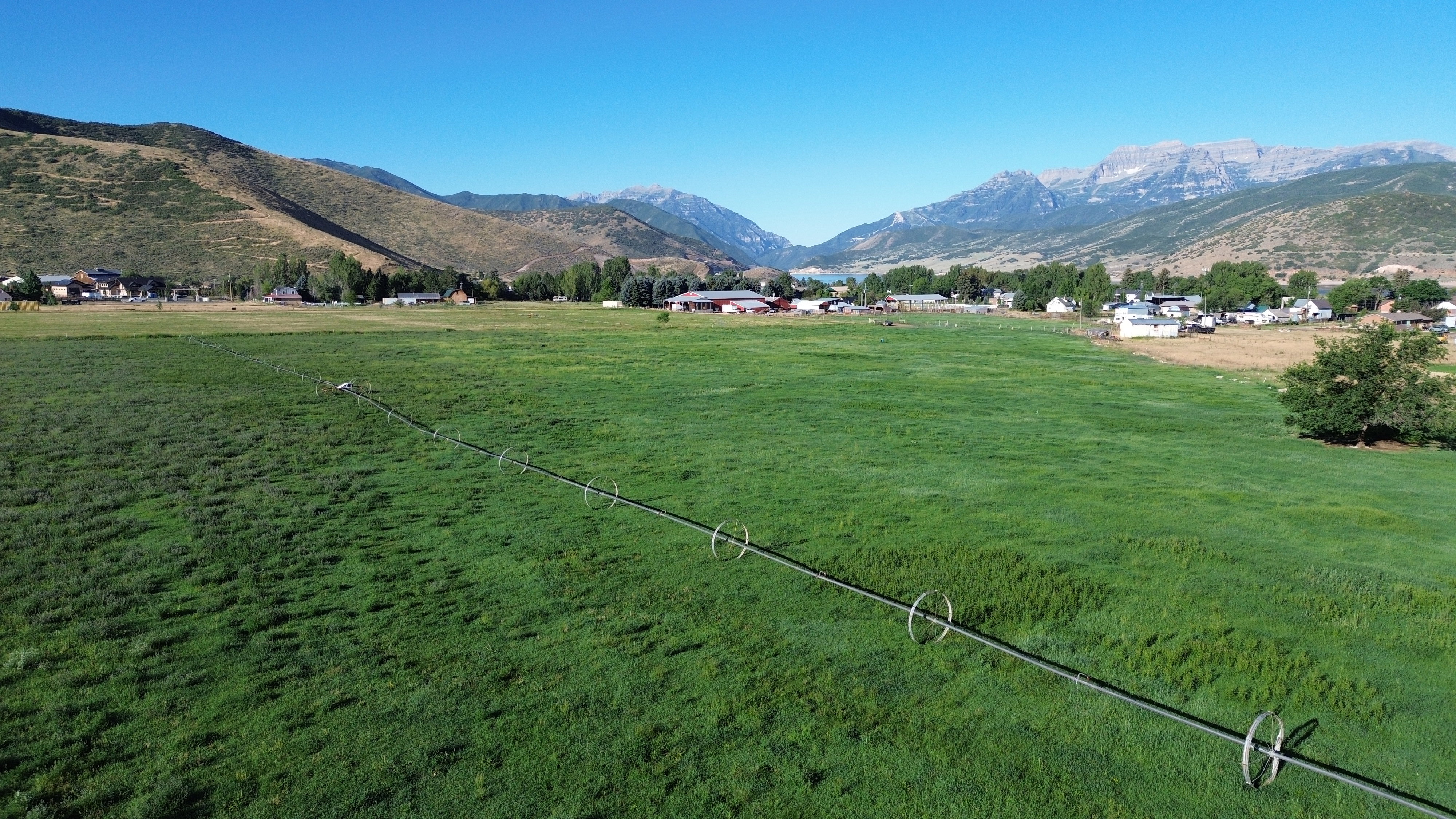 Expansive green field with an irrigation system, bordered by distant homes and mountainous terrain