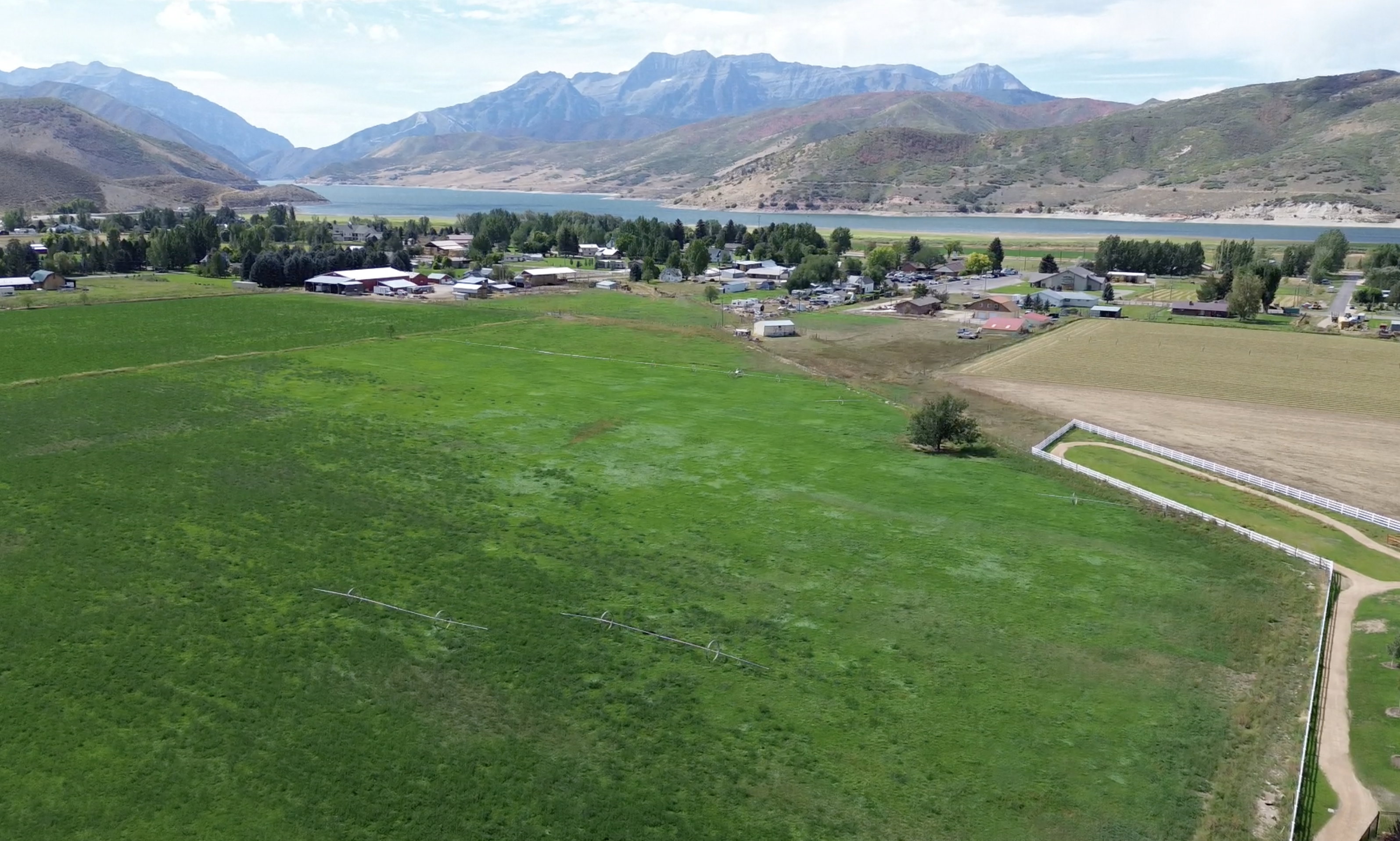 Expansive green fields with distant mountainous terrain, a body of water, and residential structures