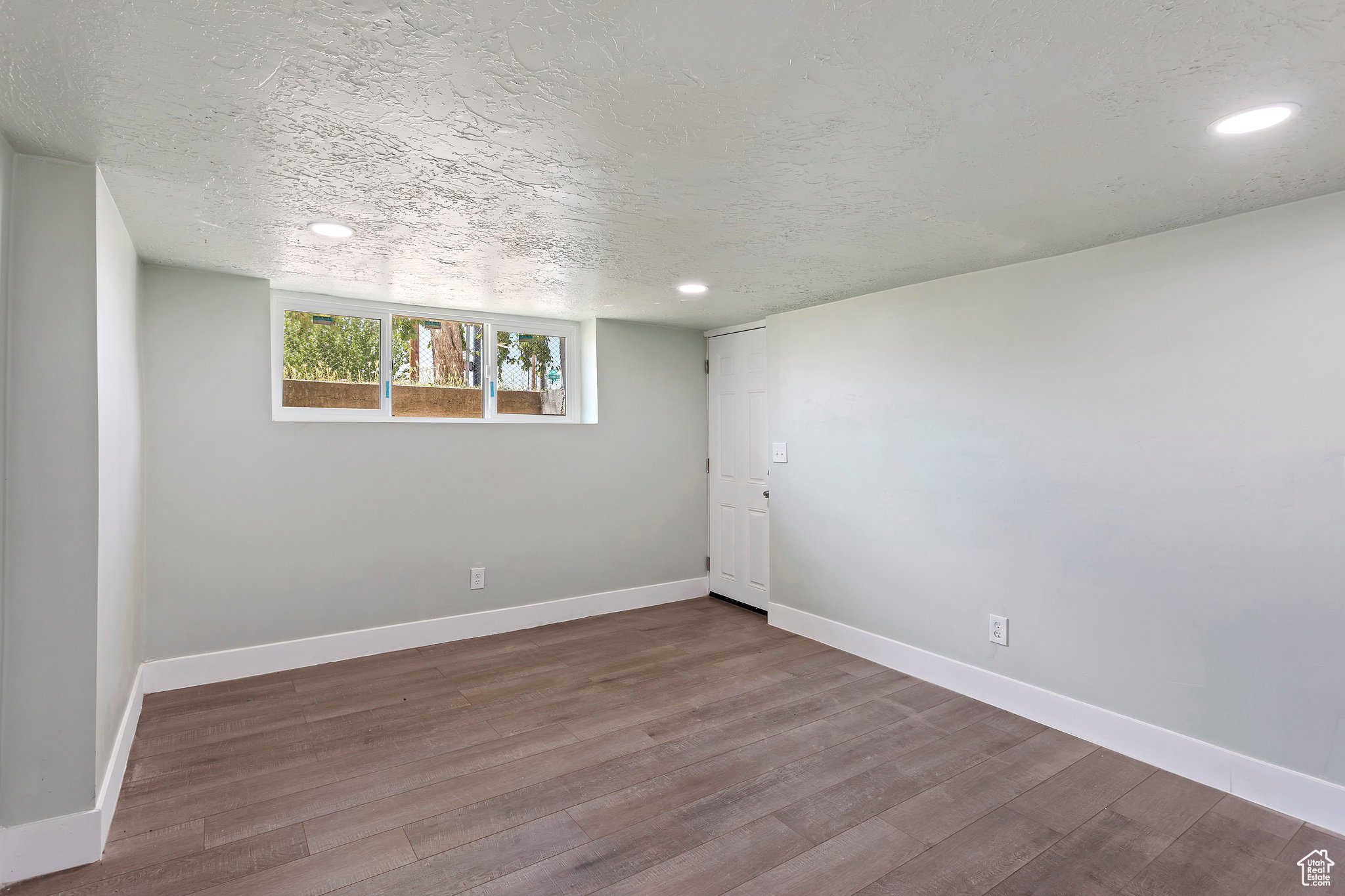Spacious room featuring wood-finish flooring, light gray walls, white baseboards, and overhead recessed lighting