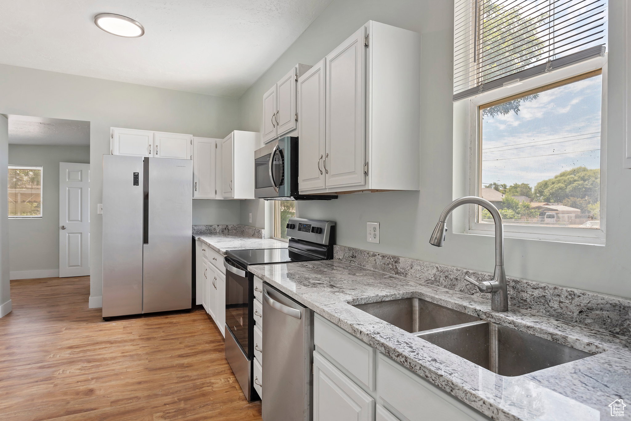 Modern kitchen featuring wood-finish flooring, white cabinetry, stainless steel appliances, and light-toned stone countertops
