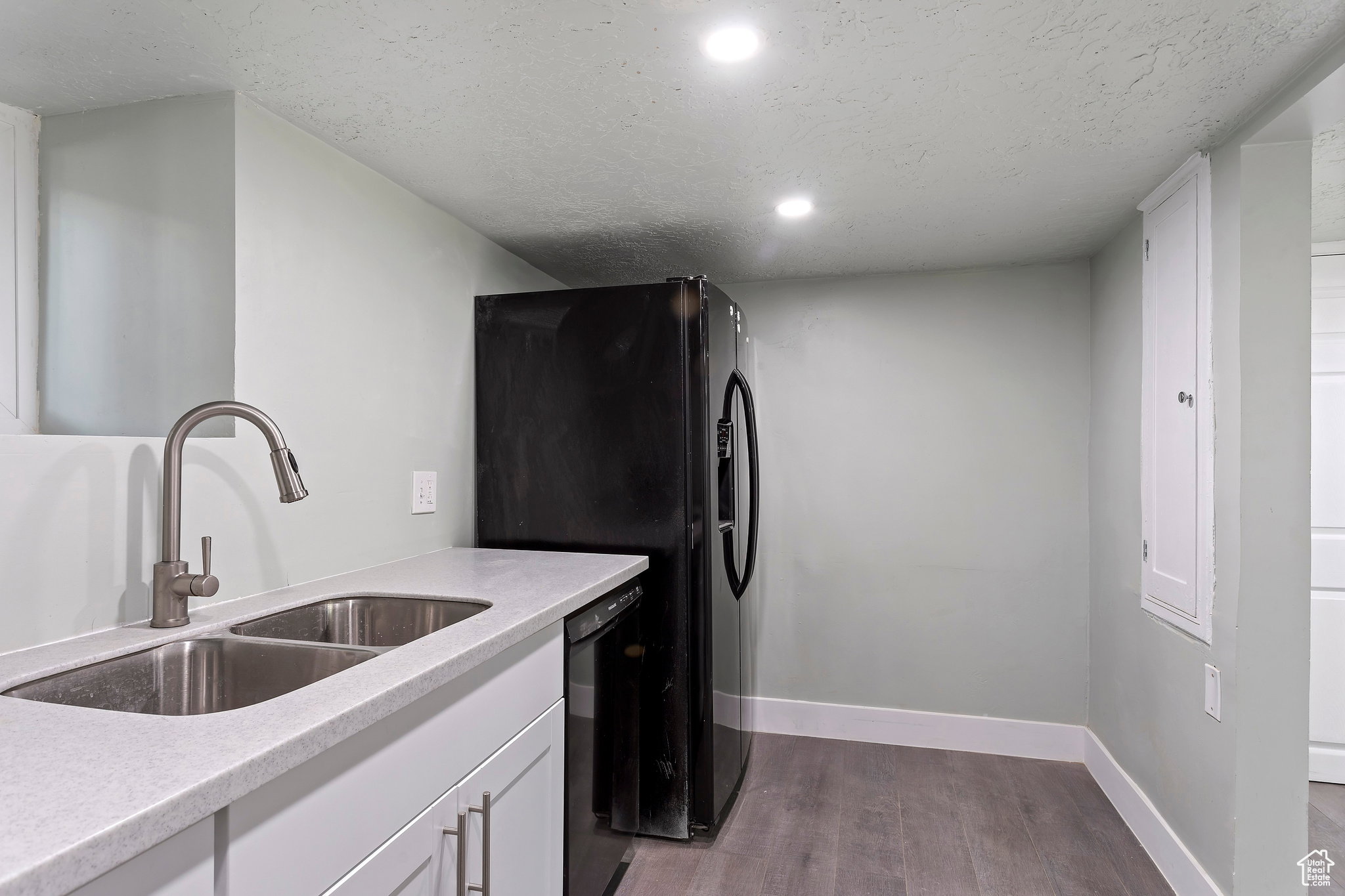 Kitchenette featuring a double basin stainless steel sink with a gooseneck faucet, light-colored countertops, white base cabinetry with brushed nickel pulls, and wood-finish flooring