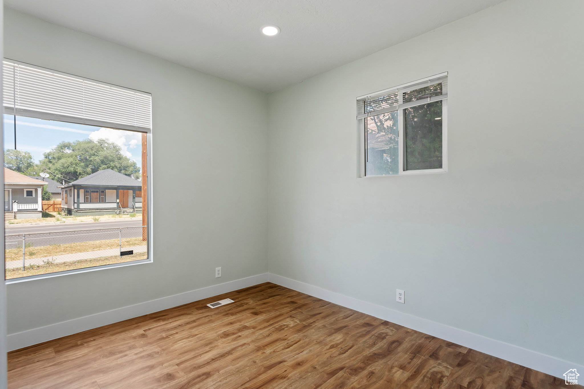 Room featuring two windows with white trim, wood-finish flooring, and light-colored walls
