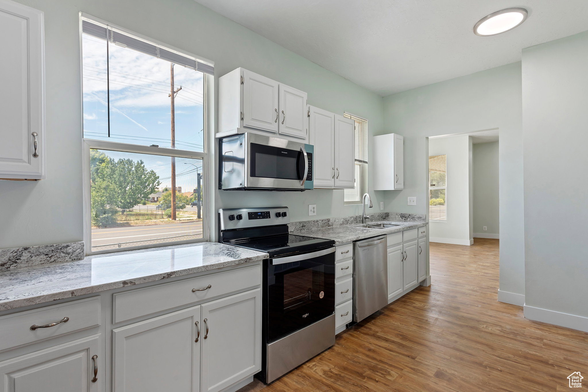 Kitchen featuring white cabinetry, stainless steel appliances, granite countertops, and wood-finish flooring