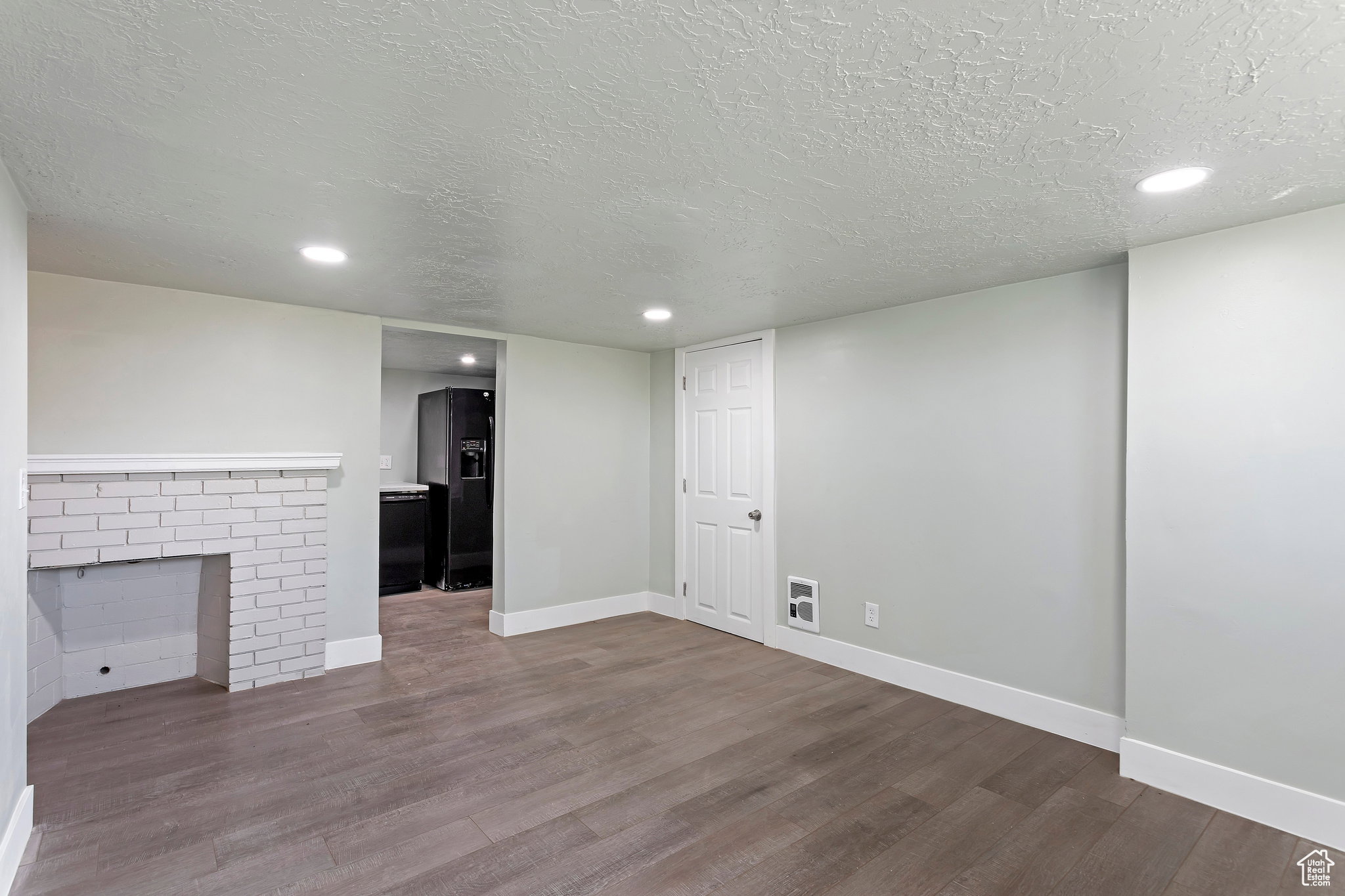 Spacious room featuring wood-finish flooring, a white brick fireplace, recessed lighting, and a white paneled door