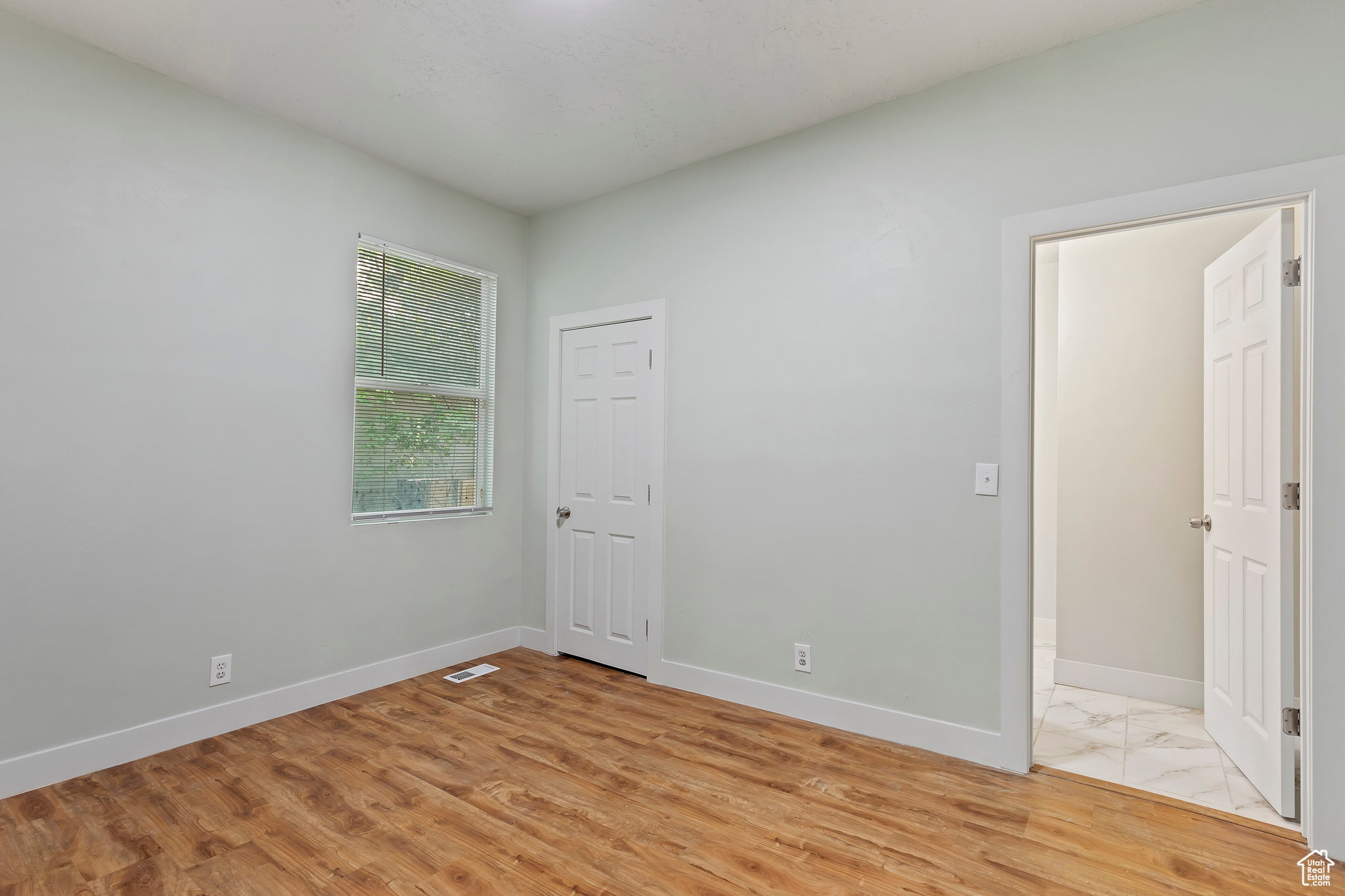 Interior space with wood-finish flooring, light-colored walls, a single window, and a paneled door