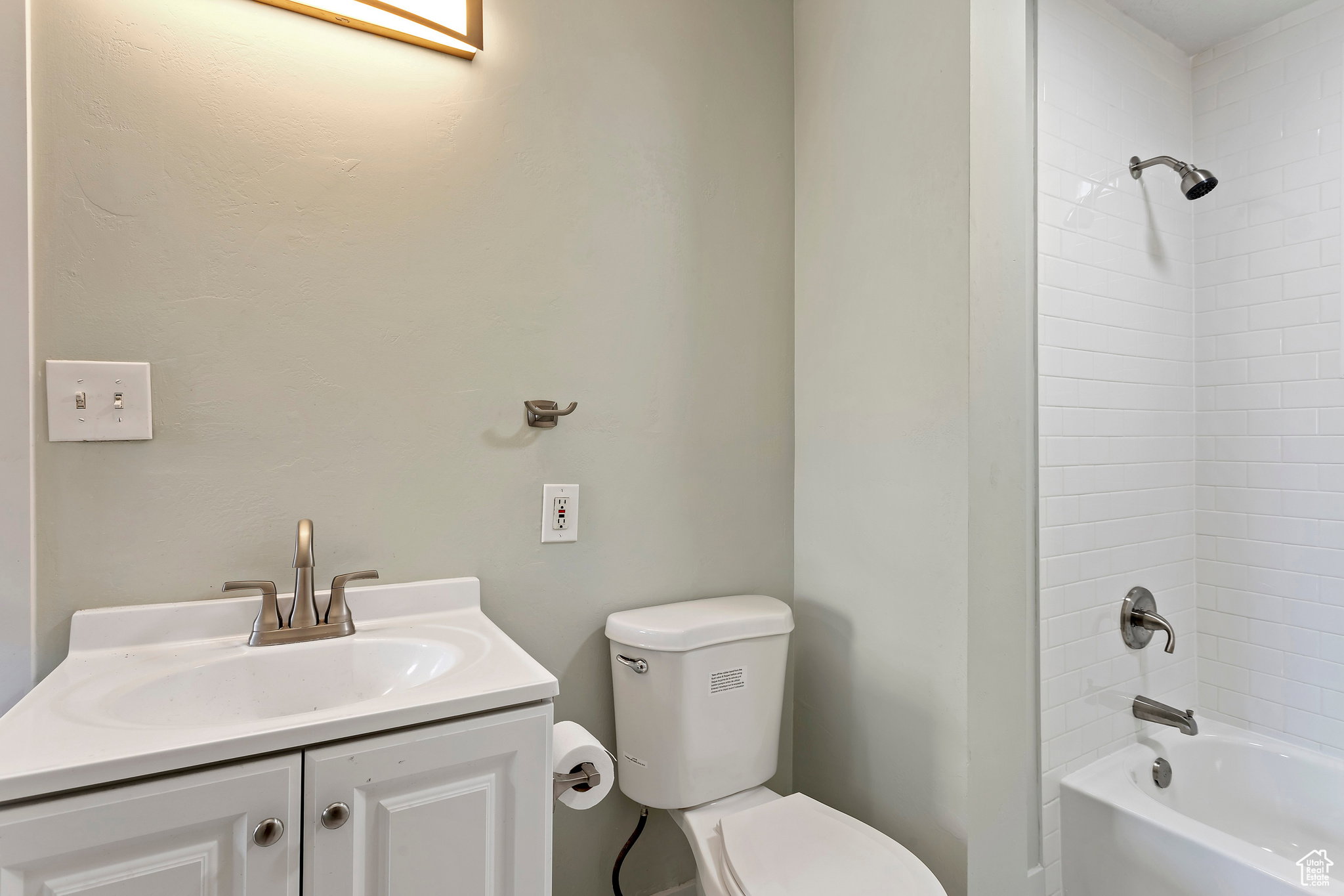 Bathroom featuring a white vanity with integrated sink, brushed nickel faucet, white subway tile shower surround, and a coordinating shower/tub combination