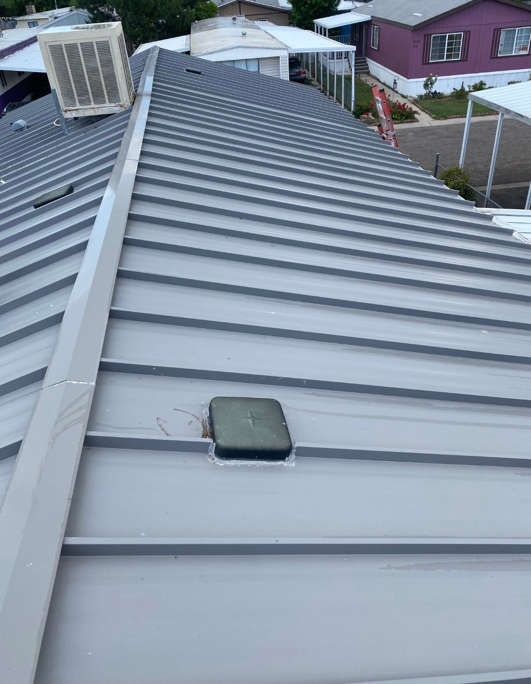 Gray corrugated metal roofing with a ridge vent and a visible swamp cooler unit