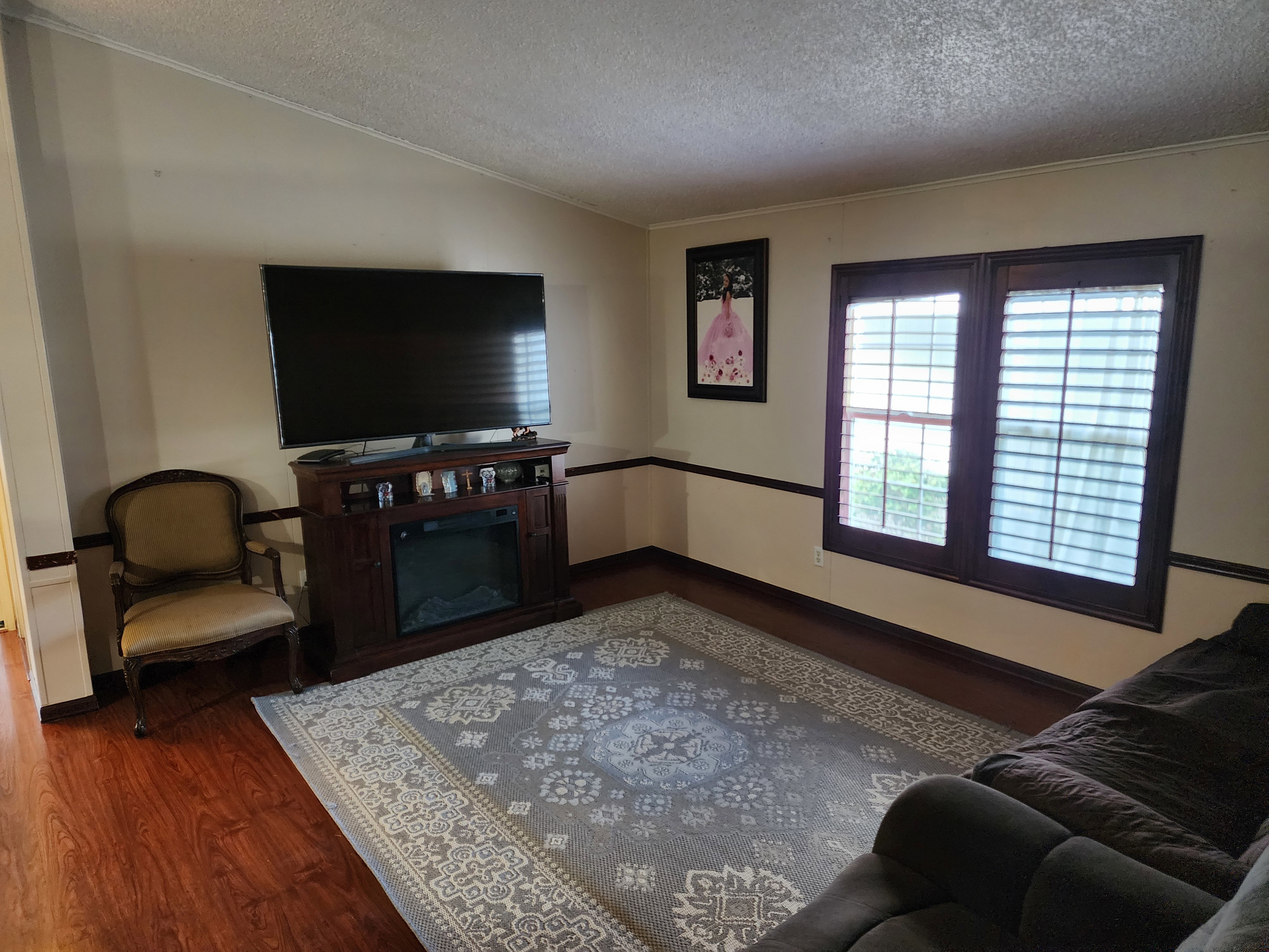 Living area featuring wood-finish flooring, an electric fireplace unit, and shuttered windows