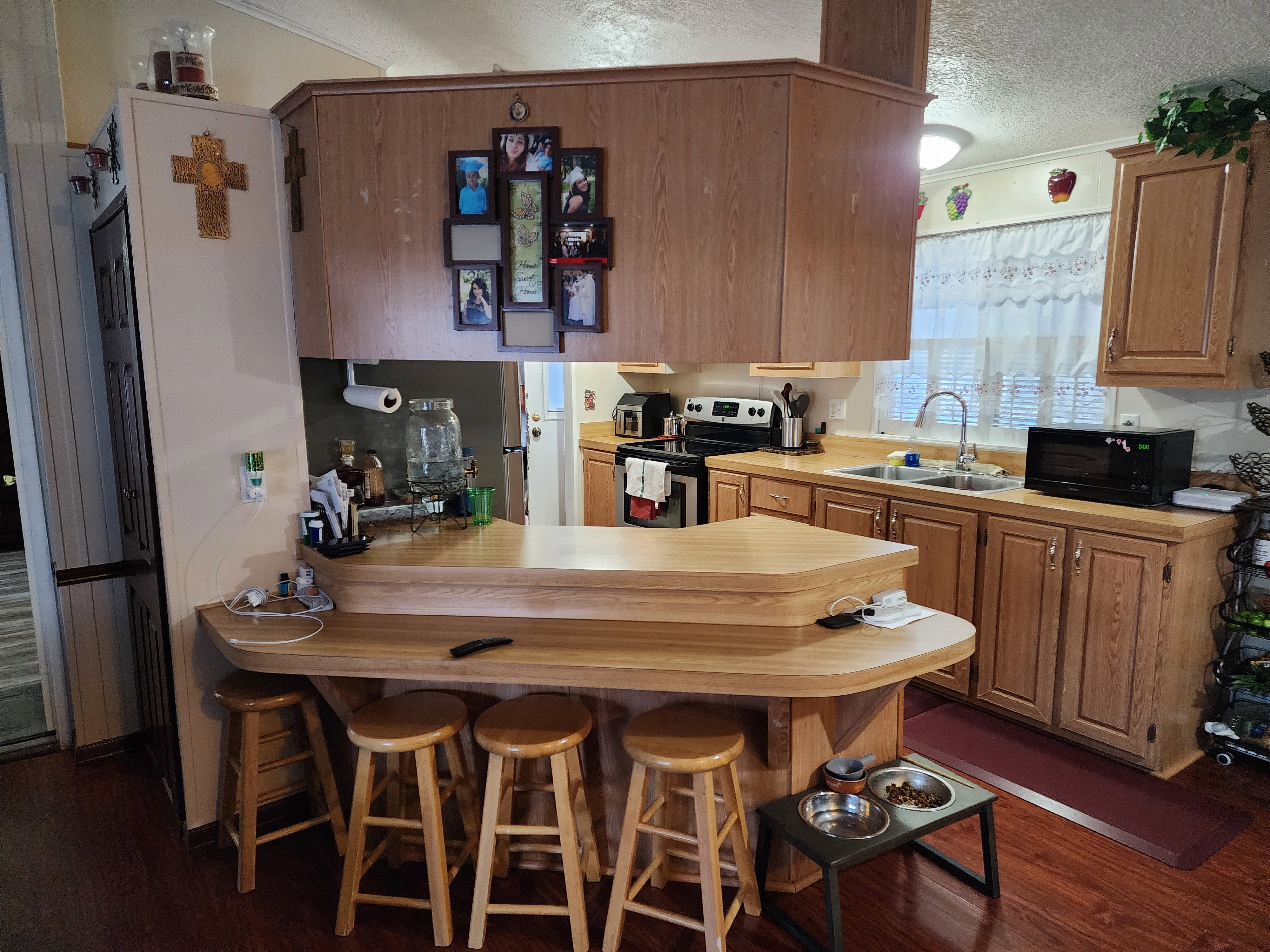 Kitchen featuring wood-finish flooring, a two-tiered breakfast bar, oak cabinetry, a double basin sink, and a window with privacy blinds