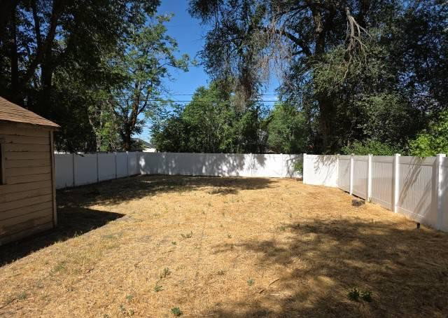 Expansive yard featuring a white privacy fence, mature trees, and a detached shed with wood siding and a shingle roof