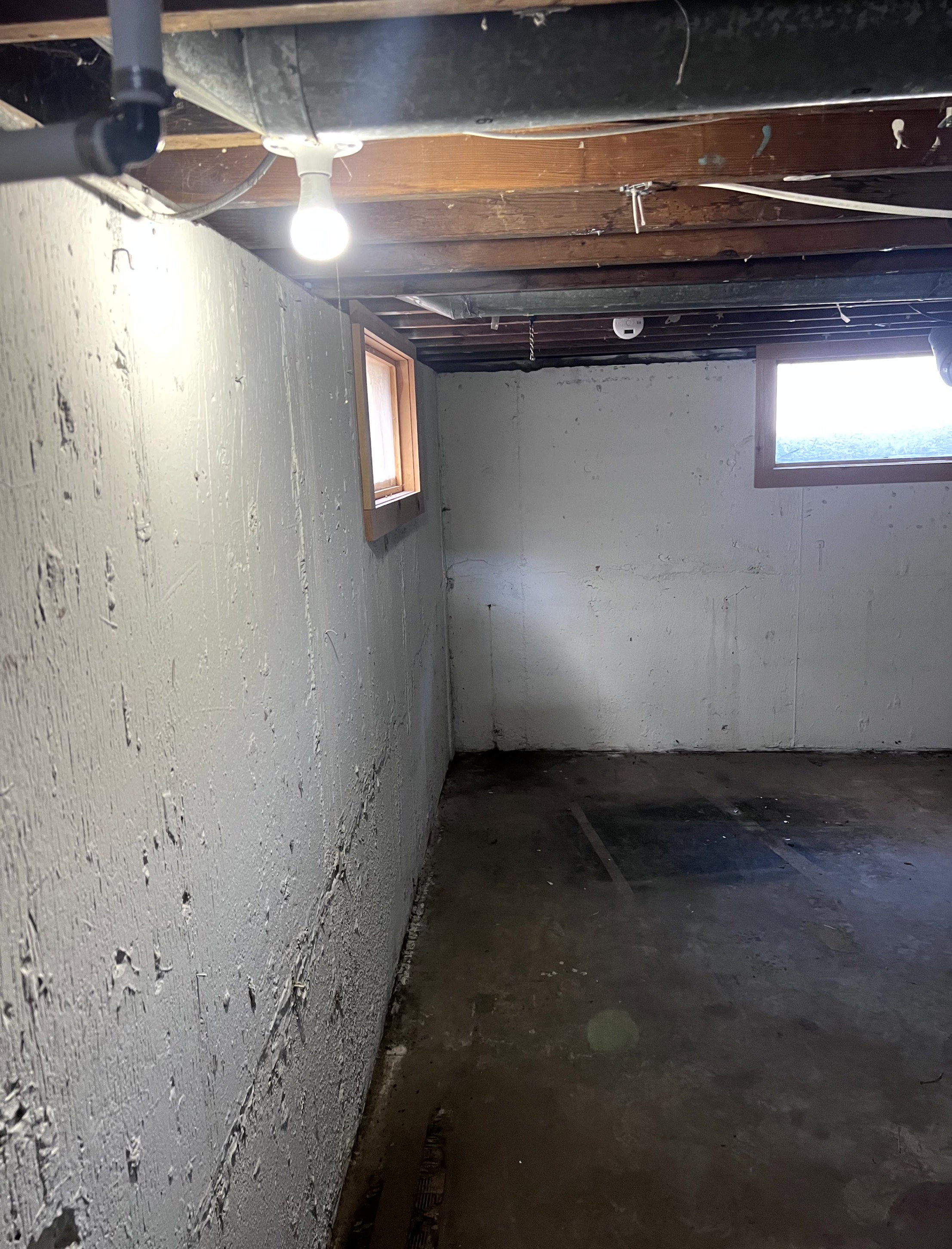 Unfinished basement space featuring exposed ceiling joists, concrete walls, two windows with wood trim, and a concrete floor
