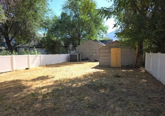 Expansive backyard featuring a white privacy fence, an accessory structure with horizontal siding, and mature trees providing shade