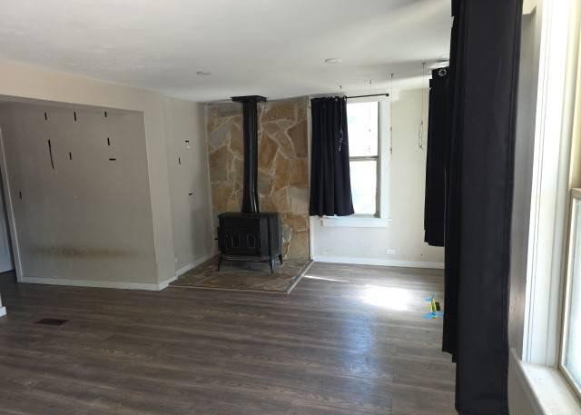 Living space featuring wood-finish flooring, a stone accent wall, and a freestanding wood-burning stove with a stone hearth