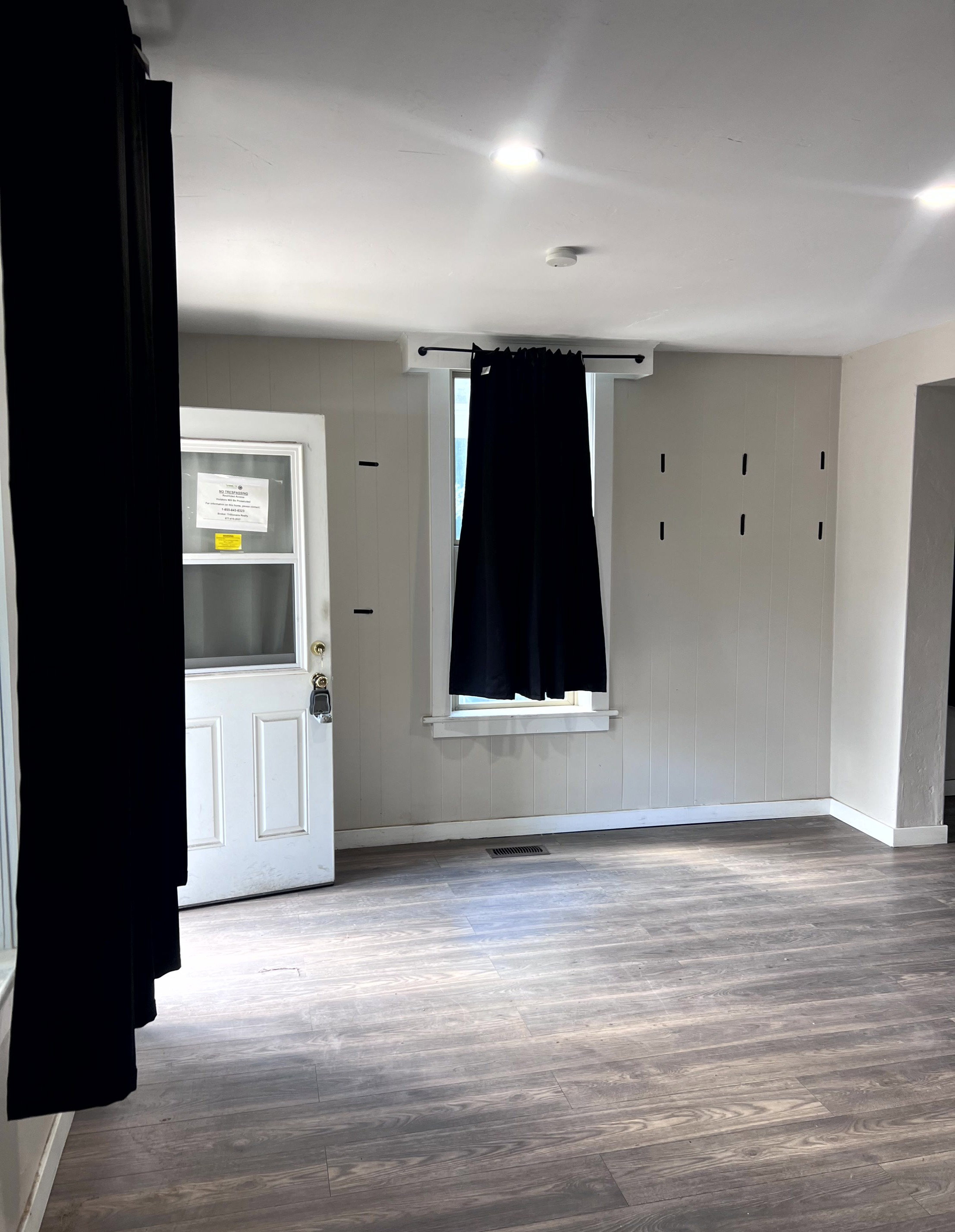Spacious room featuring wood-finish flooring, recessed lighting, and a white paneled entry door with a storm door