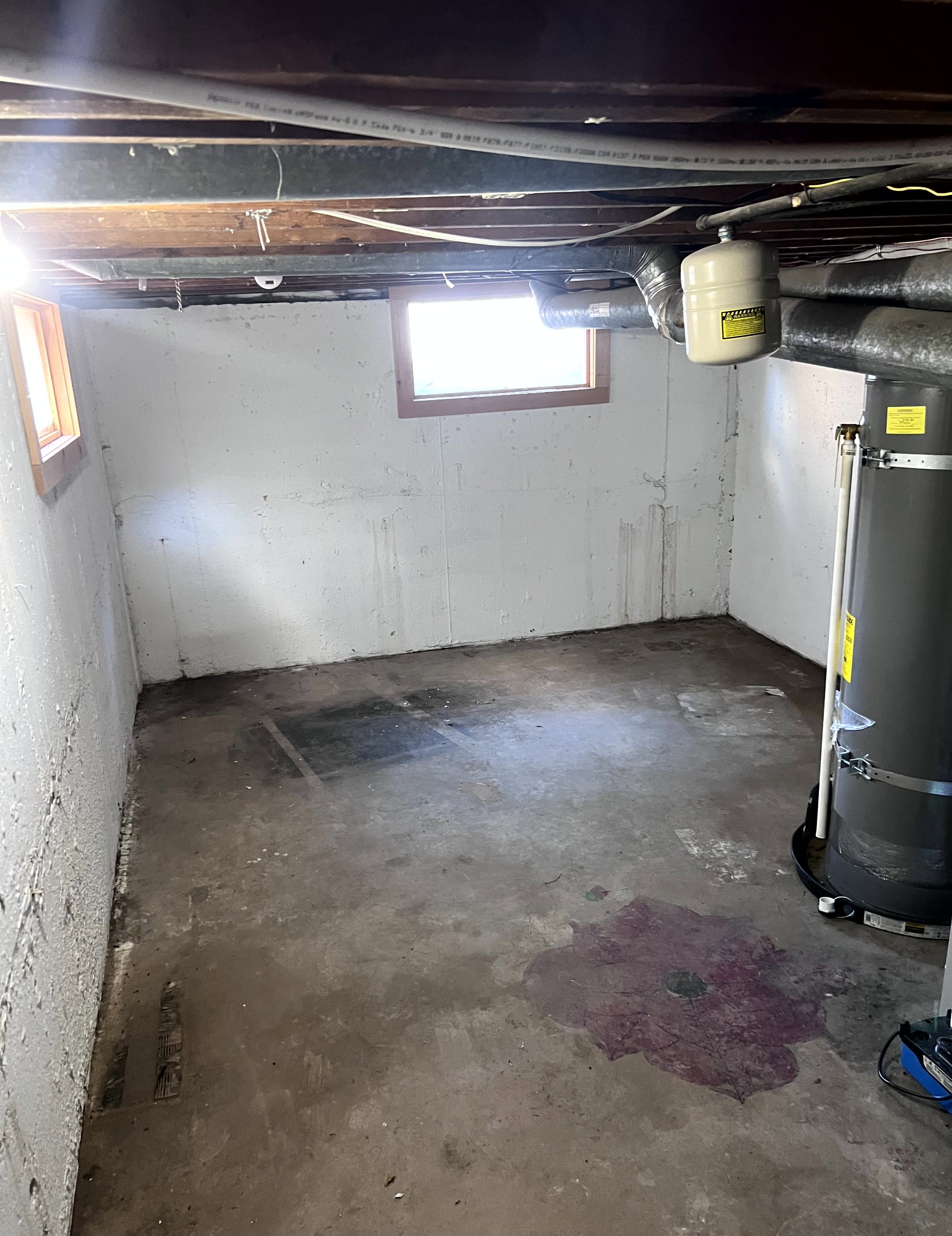 Unfinished basement space featuring concrete walls, exposed ceiling joists, and two small windows