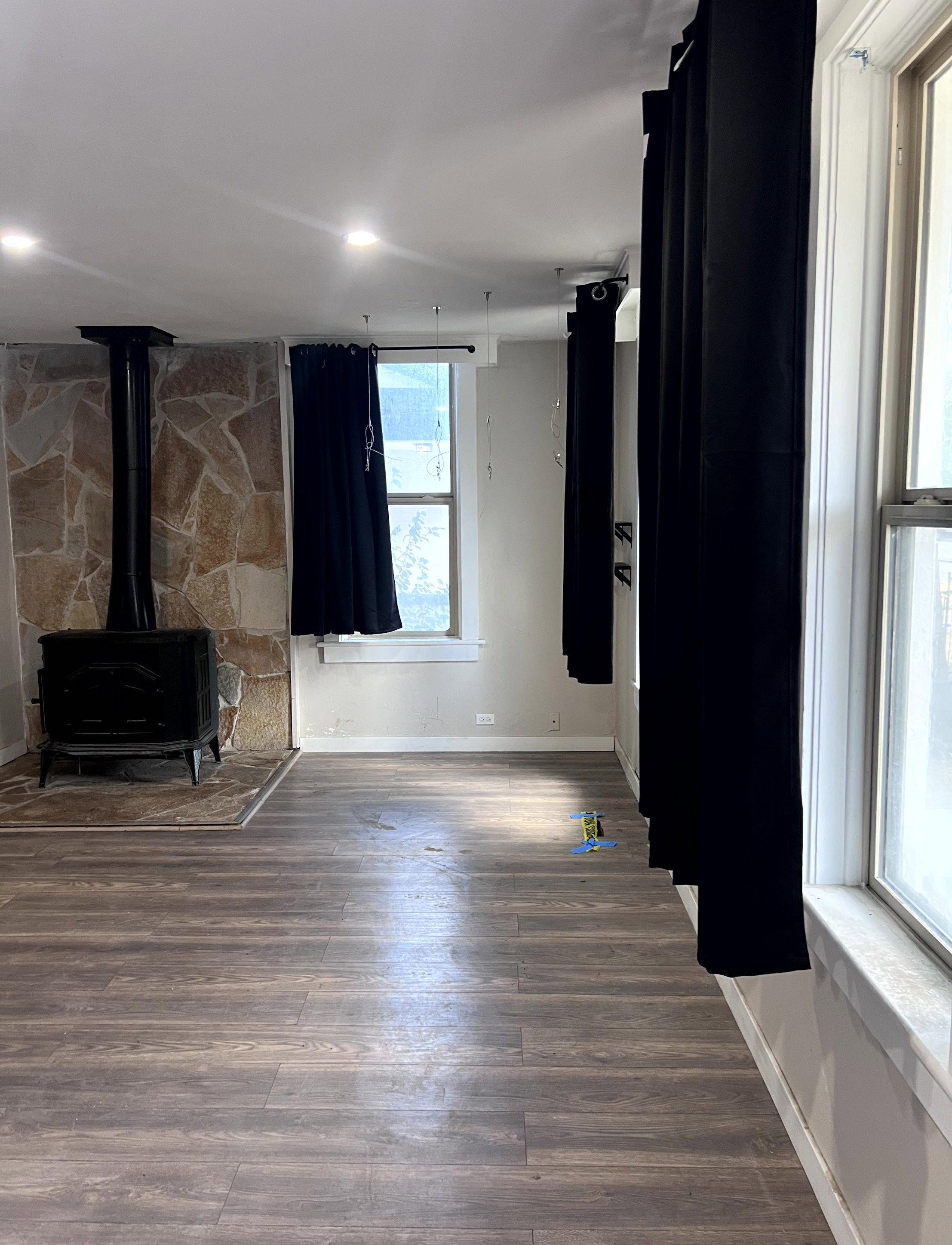 Room featuring a cast-iron stove with a stone surround, wood-finish flooring, recessed ceiling lighting, multiple windows, and light-toned walls