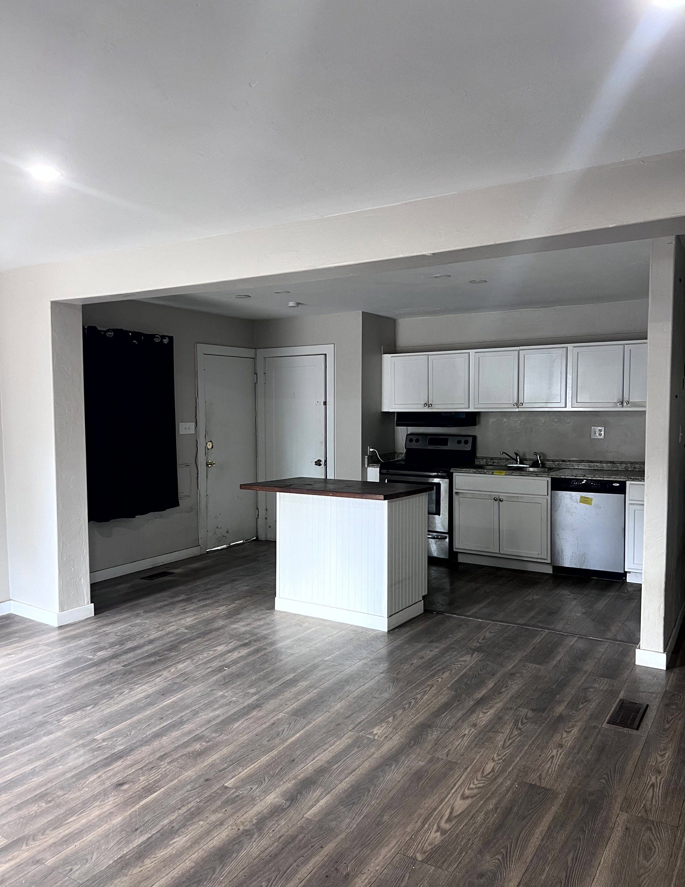 Open-concept living area featuring wood-finish flooring, recessed lighting, and a white kitchen island with a dark countertop