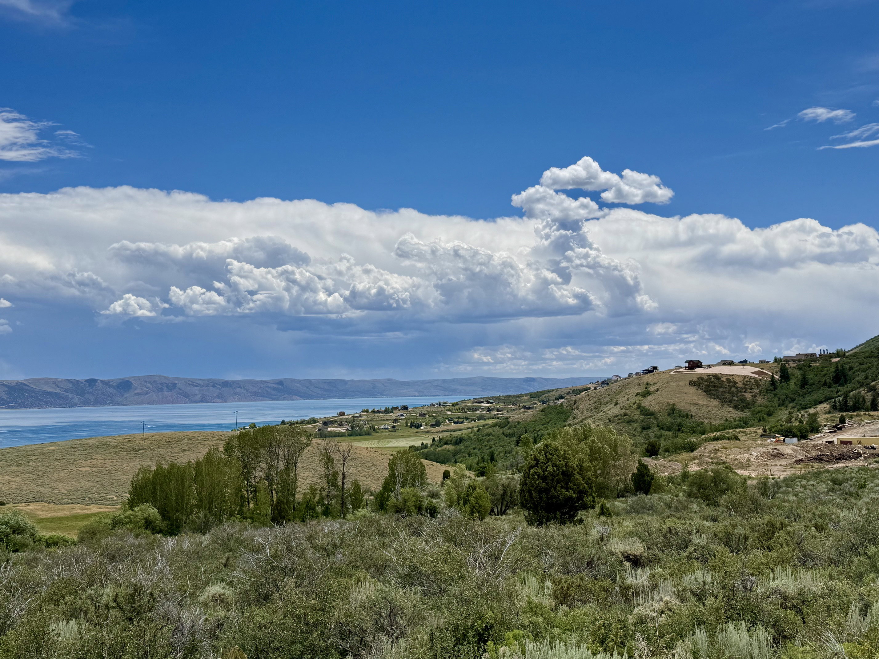 Expansive landscape featuring a large body of water, distant hills, and diverse natural vegetation