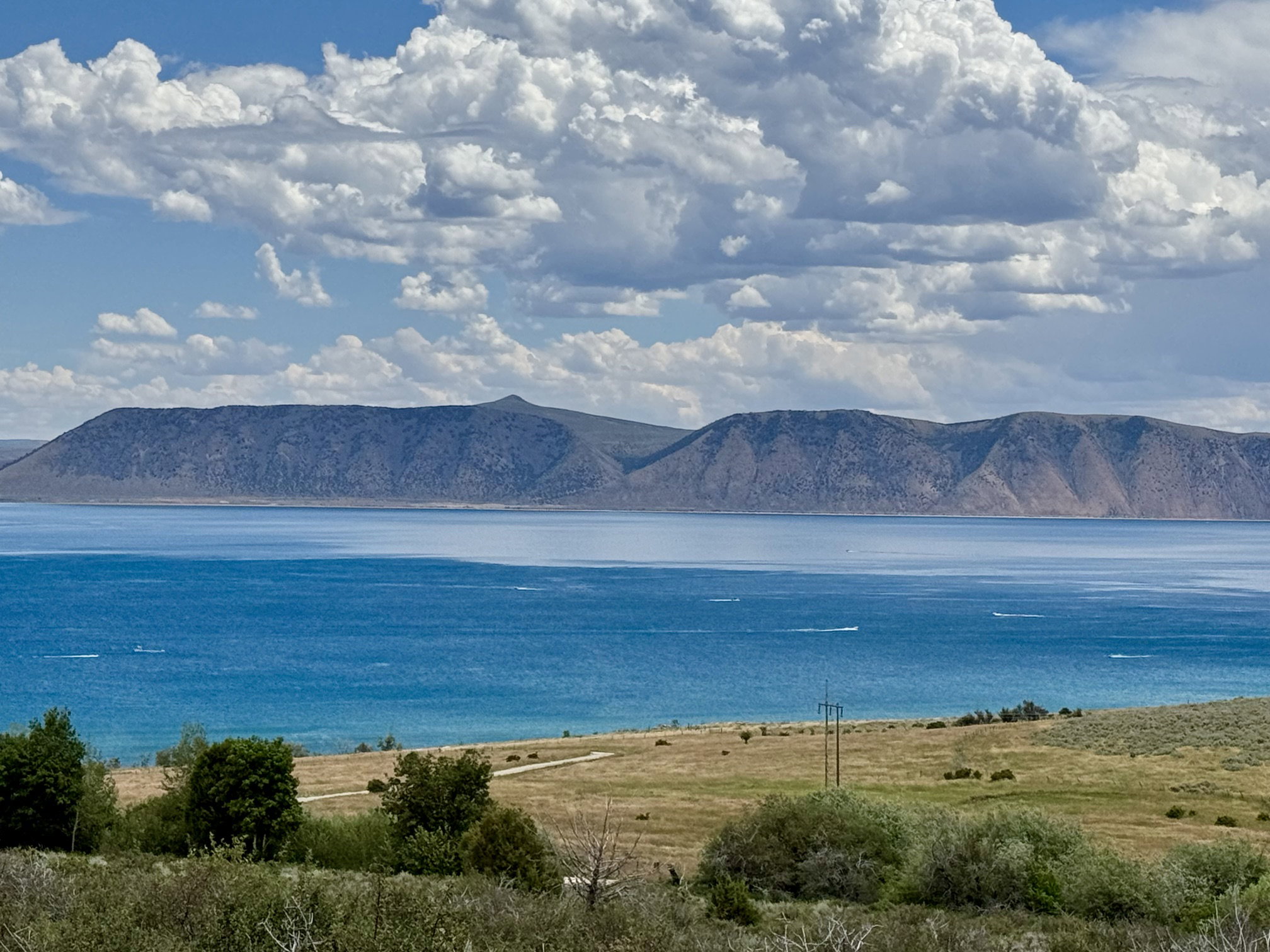 Expansive water body with distant mountain ranges under a sky with prominent clouds
