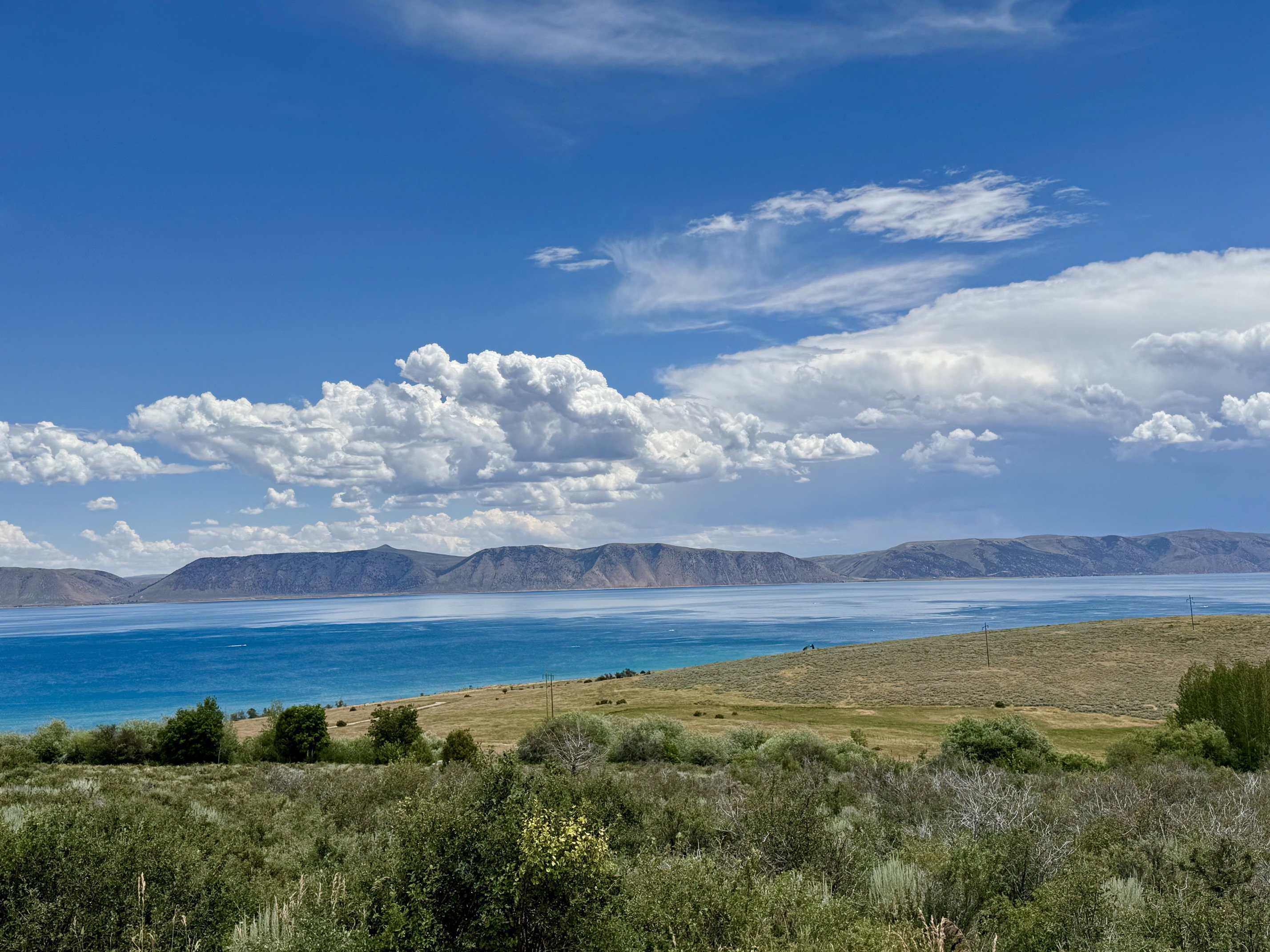 Expansive water frontage featuring a vibrant blue lake, distant mountain range, and natural shrubland