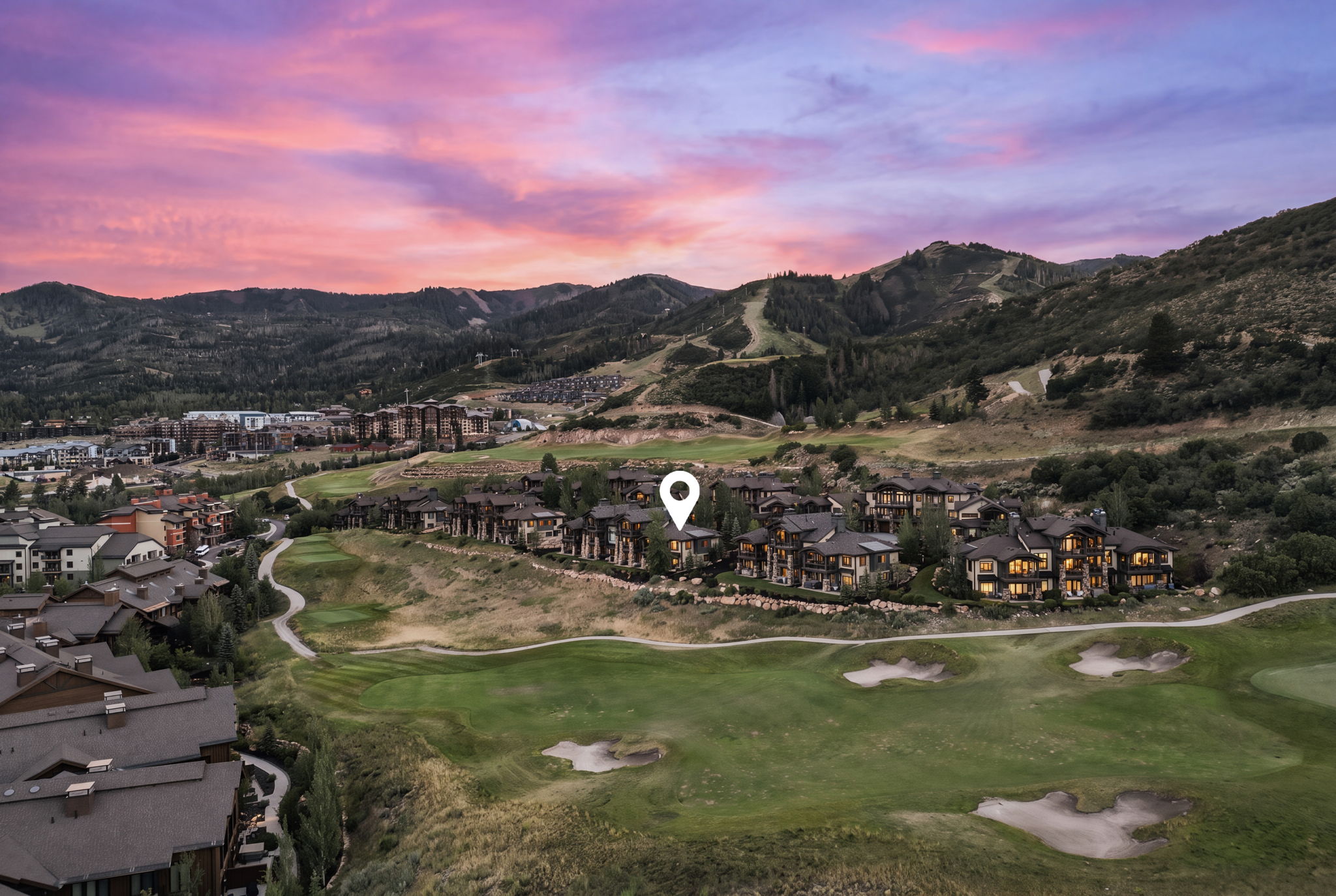 Expansive mountain landscape featuring a golf course, surrounding residential structures, and forested hillsides