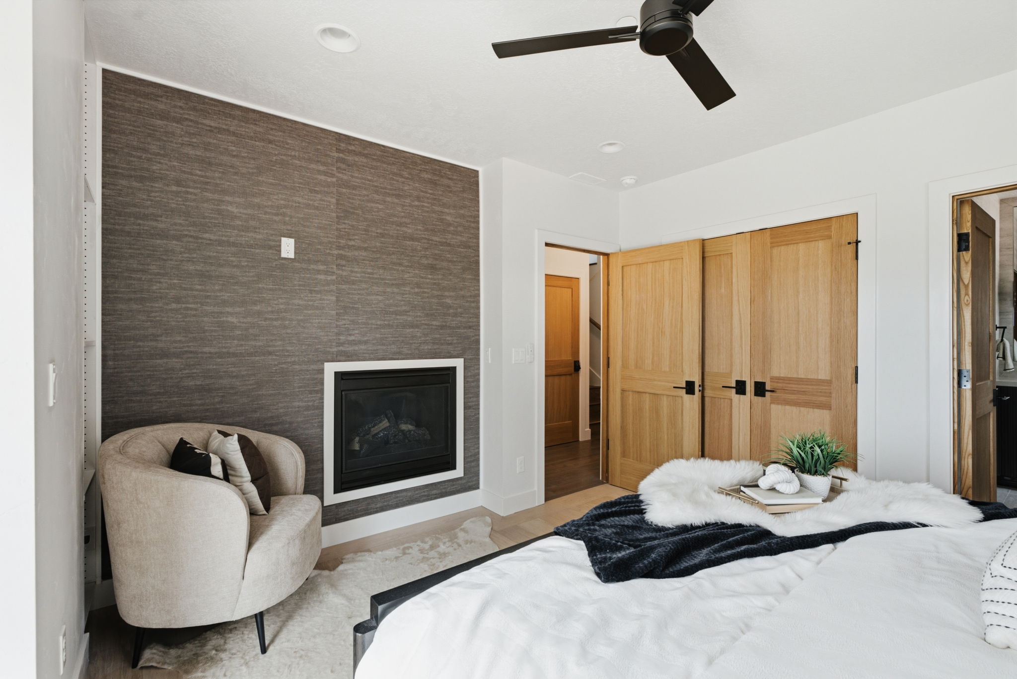 Accent wall featuring a built-in fireplace, a ceiling fan, light oak wood doors with black hardware, and light wood-finish flooring