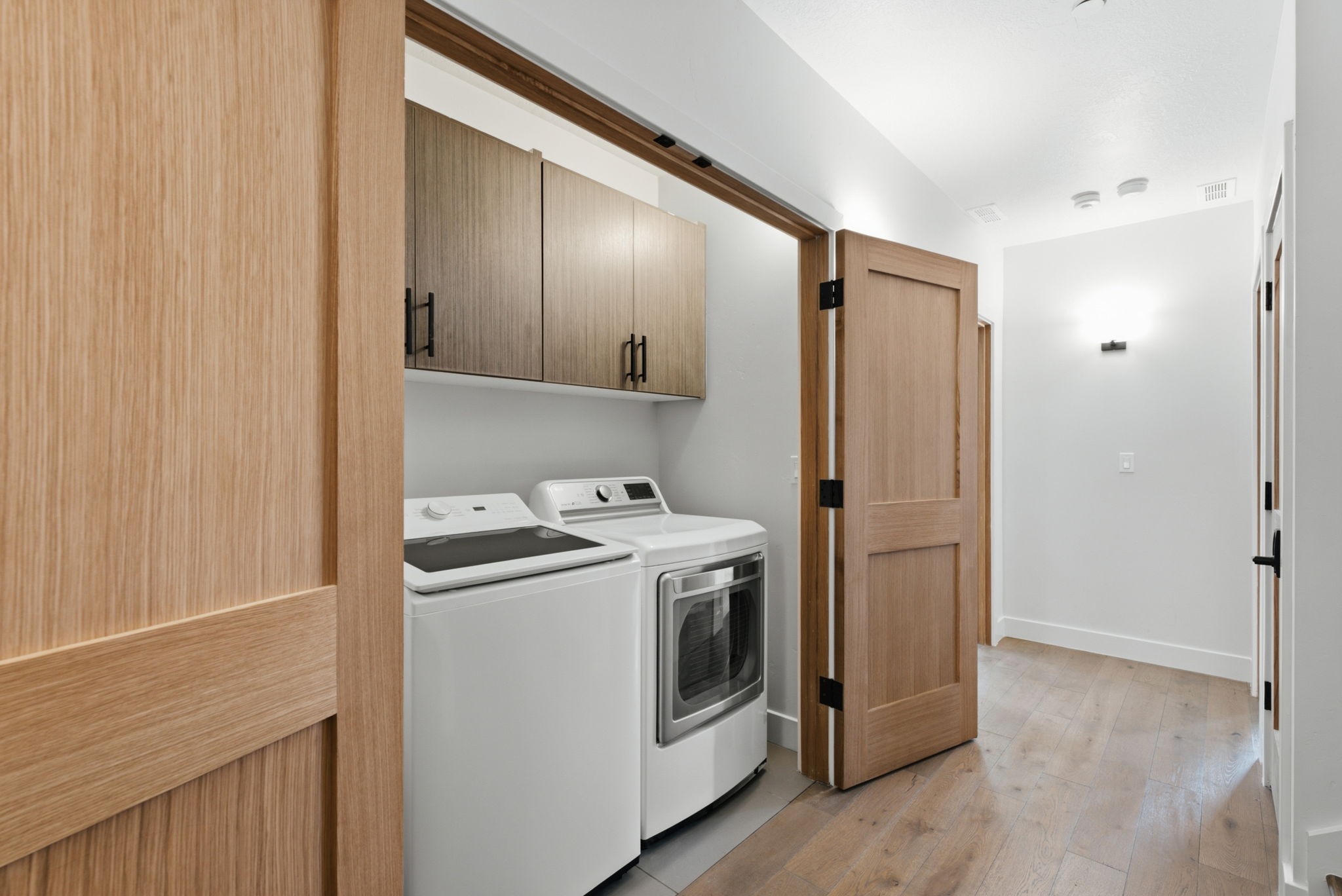 Laundry area w/ washer & dryer, wood-finish flooring, built-in cabinetry with matte black hardware, and an open-concept hall with recessed lighting