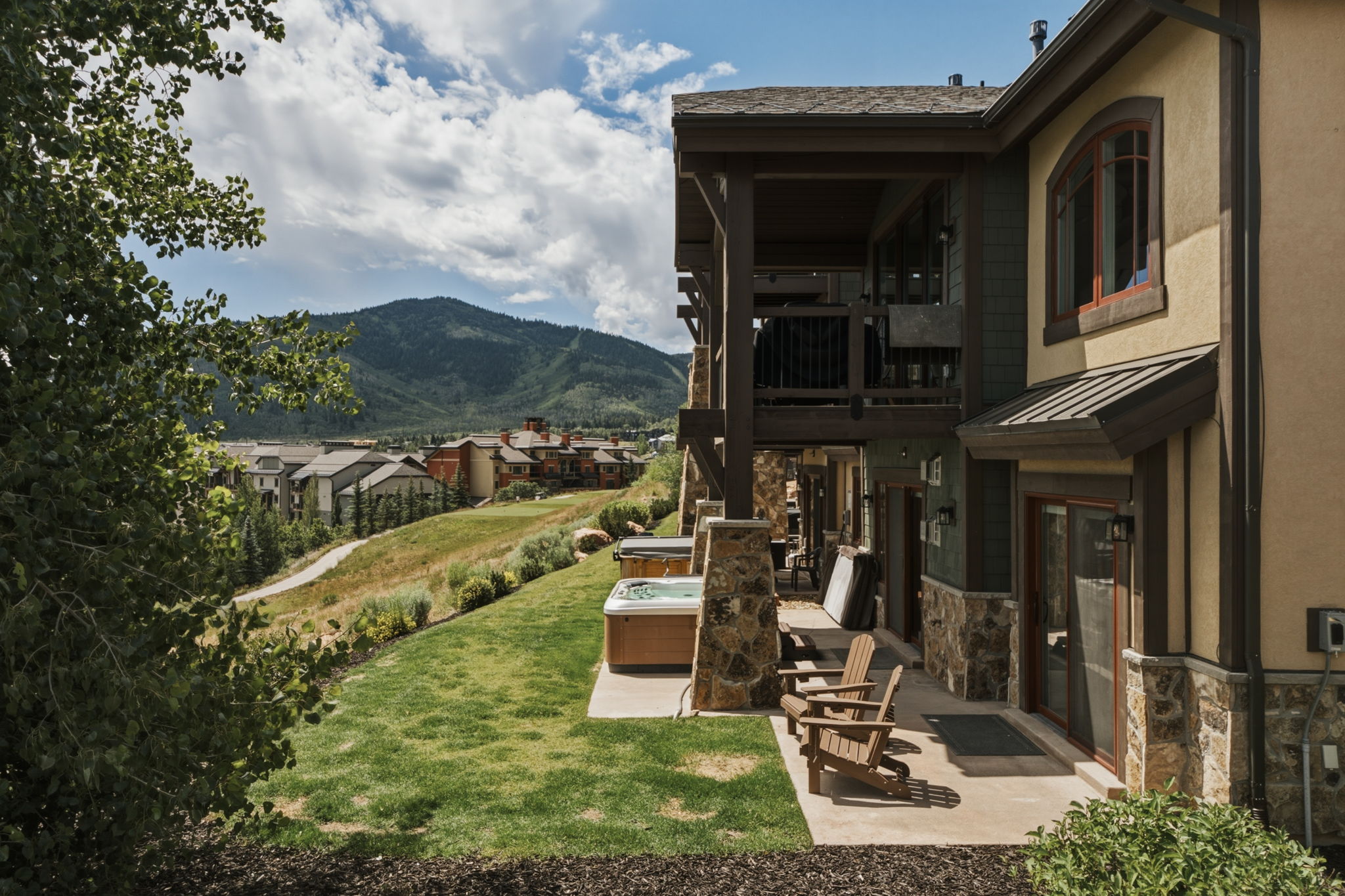 Rear exterior featuring two levels of outdoor living spaces, a ground-level patio with hot tub, and a second-level covered balcony